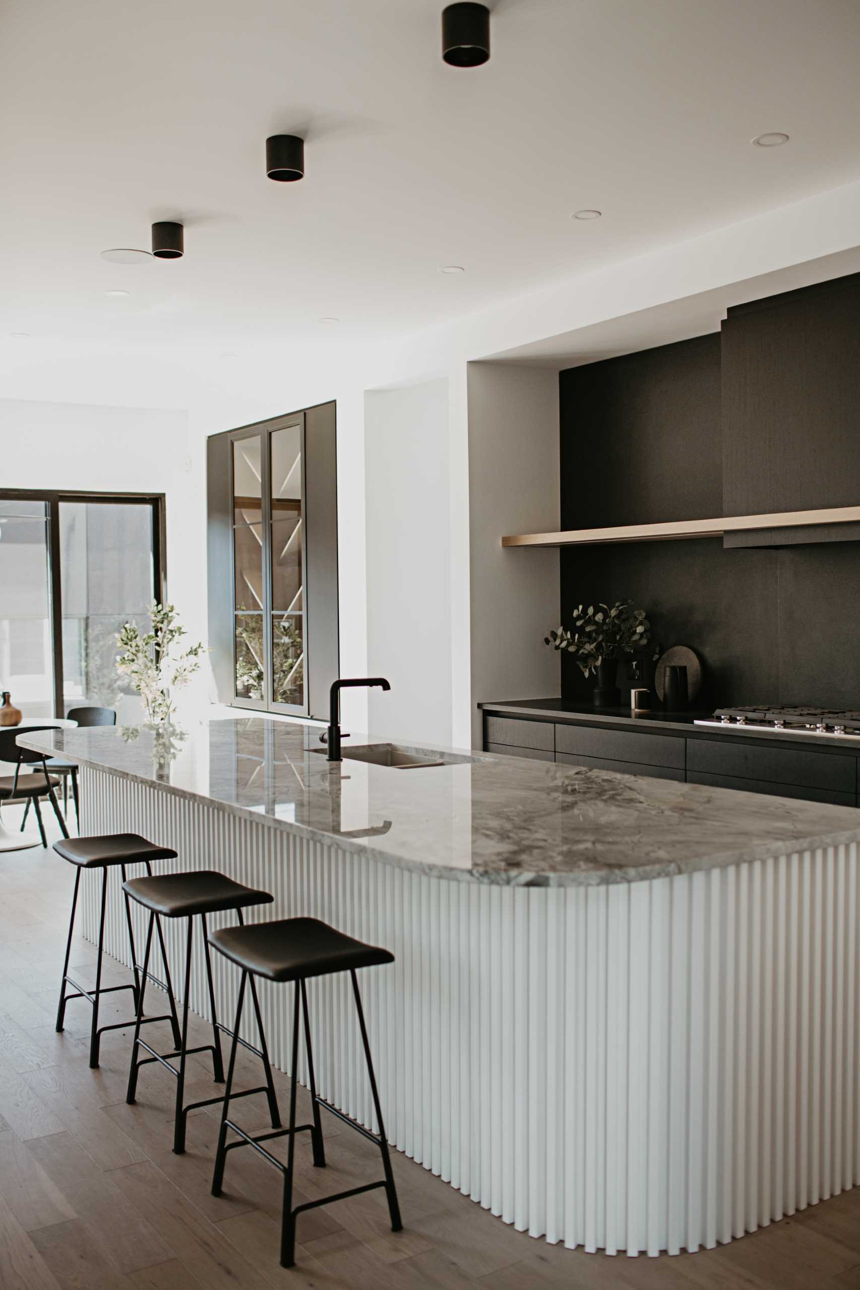 The design of this modern kitchen has a highly contrasting black and white look. To soften the starkness, a curve in the super white dolomite countertop on the island is replicated onto a base with painted wood slats.