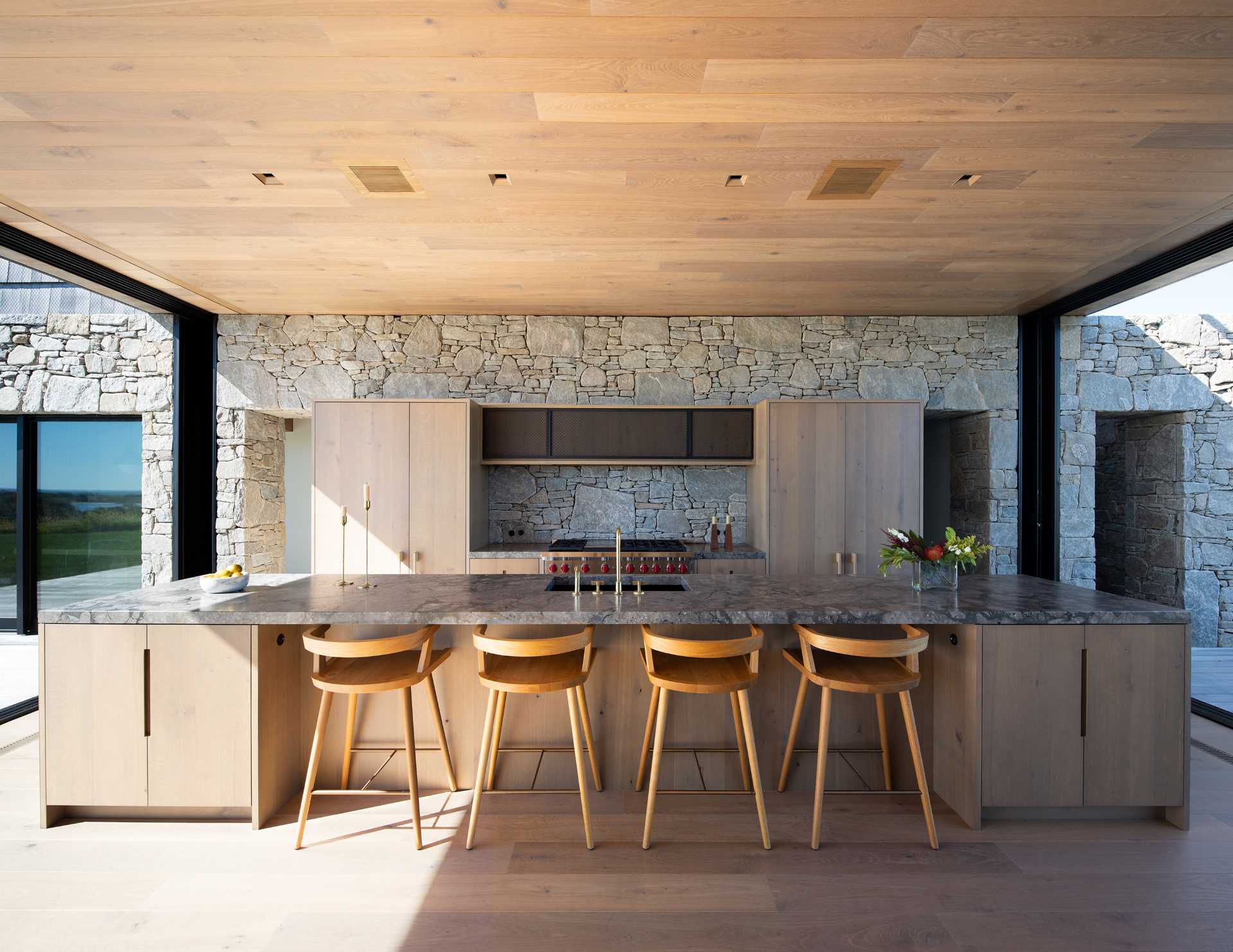 A modern kitchen with a stone wall that travels from the interior to the exterior of the home.