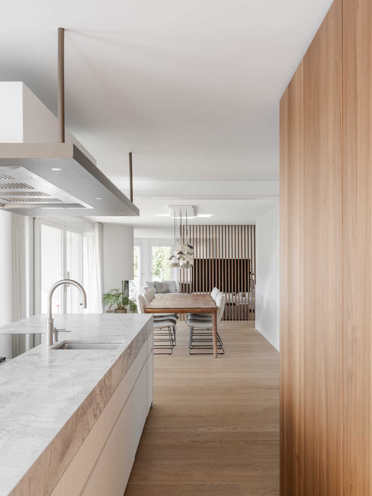 A modern kitchen with wood cabinets, wood floors, and a long kitchen island with a stone waterfall countertop.