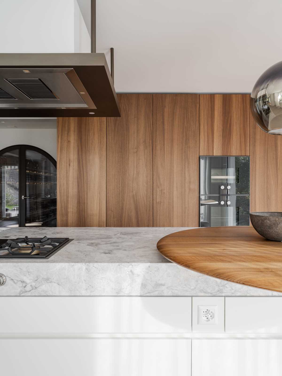 A modern kitchen with wood cabinets, wood floors, and a long kitchen island with a stone waterfall countertop.