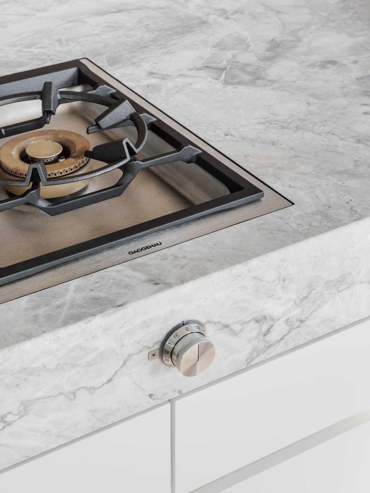 A modern kitchen with an island that includes a stone waterfall countertop and white cabinets.