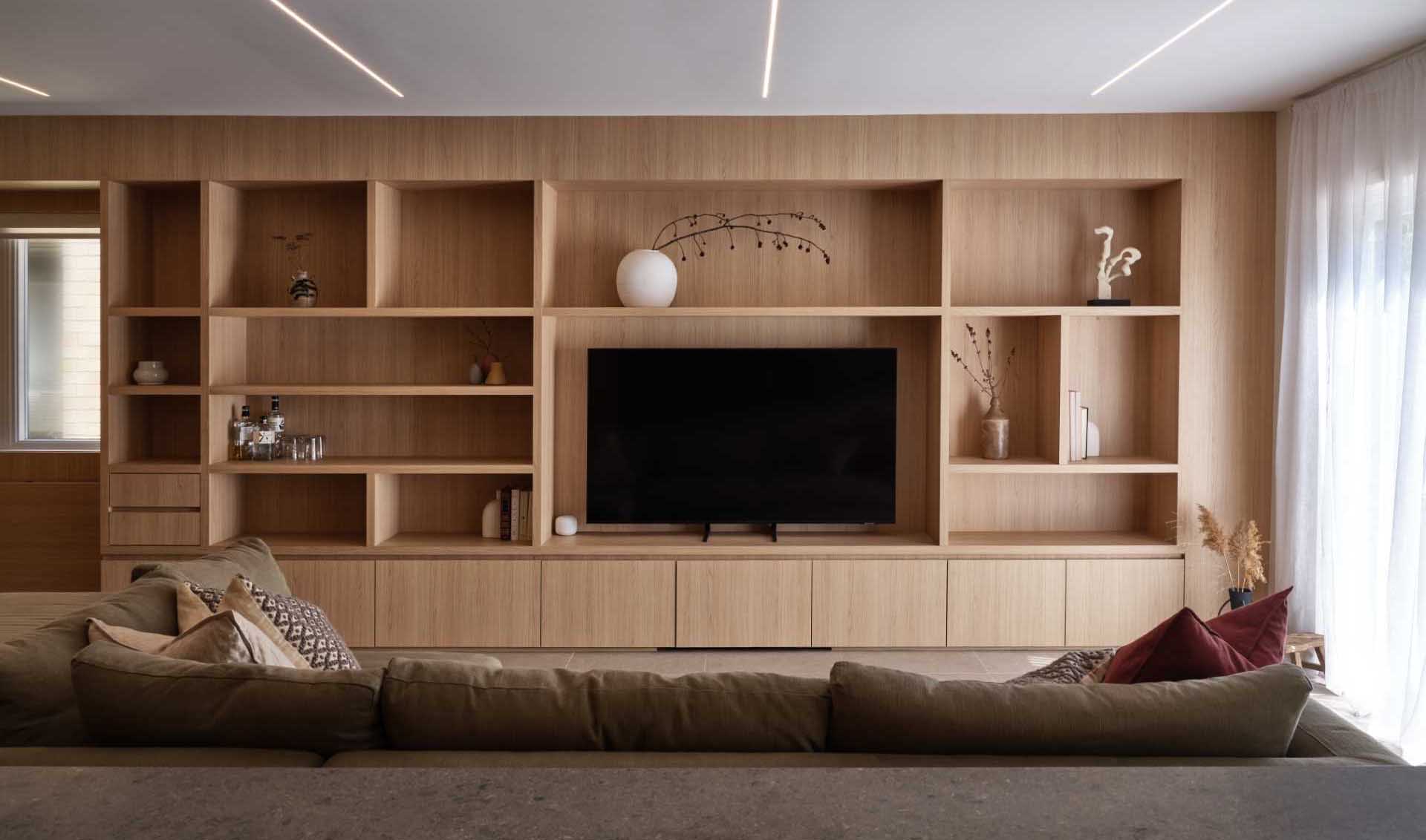 The living room and workspace are designed with wooden millwork, which surrounds the television and integrates storage, display, and flip-down tables.