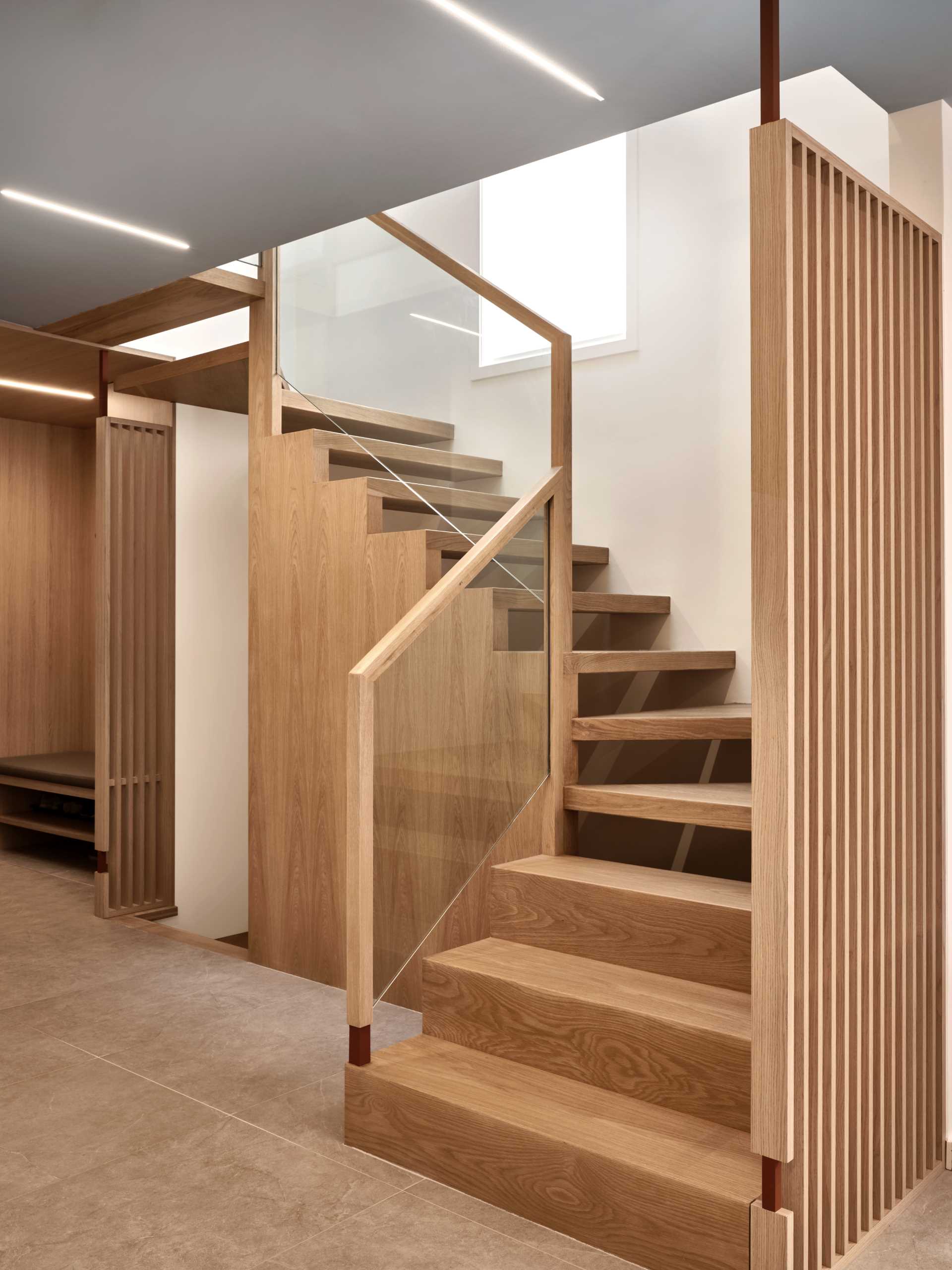 A floating staircase, which is by the foyer, combines wood and glass, while the wood panel stair wall not only acts as a privacy panel that marries the structural support of the stair but also captures the shadows casting off the steps.