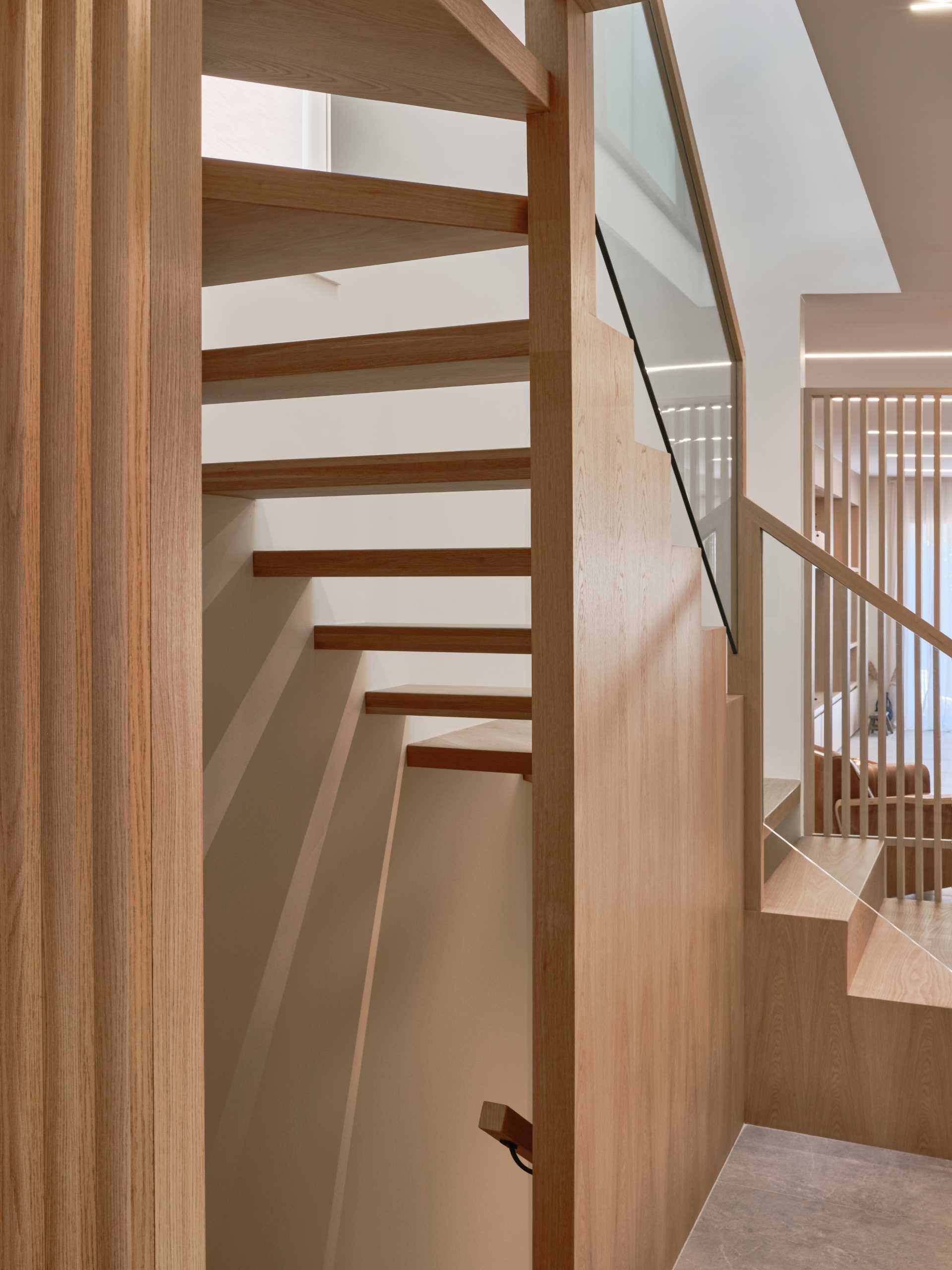 A floating staircase, which is by the foyer, combines wood and glass, while the wood panel stair wall not only acts as a privacy panel that marries the structural support of the stair but also captures the shadows casting off the steps.