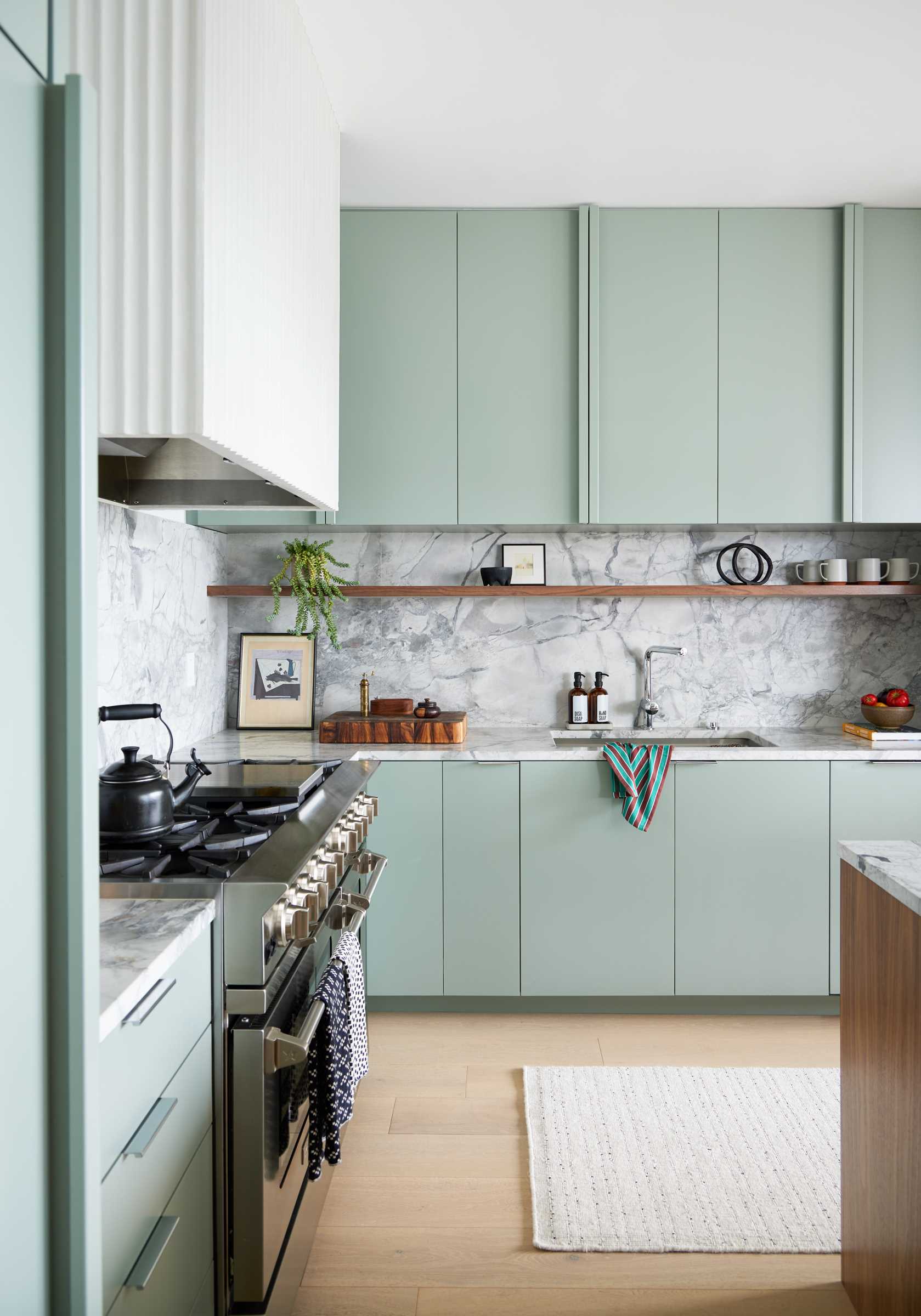 The remodeled kitchen and dining area includes a lighter palette overall, with white oak flooring, soft, creamy green cabinetry in the color of Benjamin Moore’s Rushing River, and Dolomite countertop and backsplash.