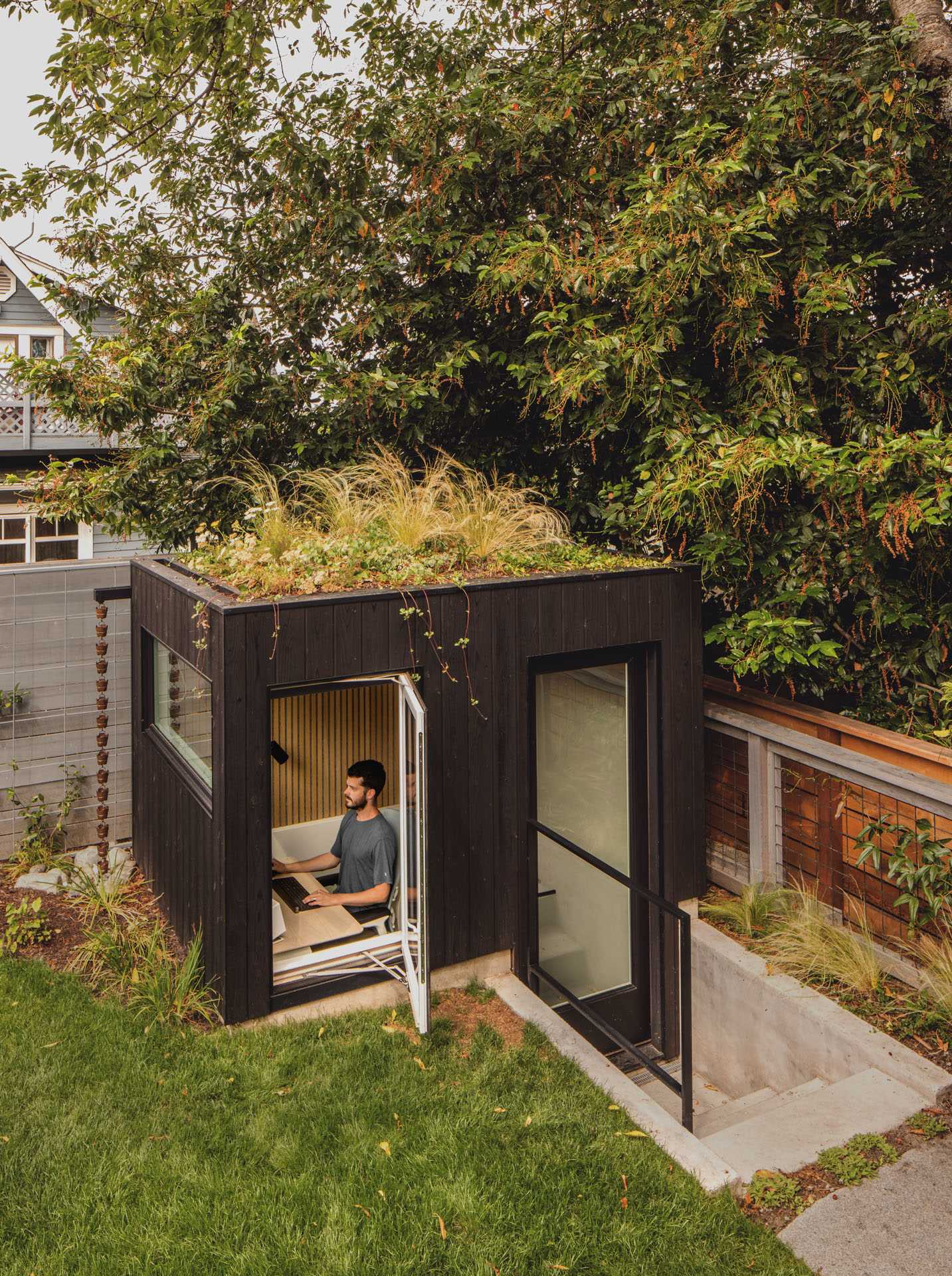 A detached work-from-home office, nestled into the backyard and partially sunken, that showcases a green roof.