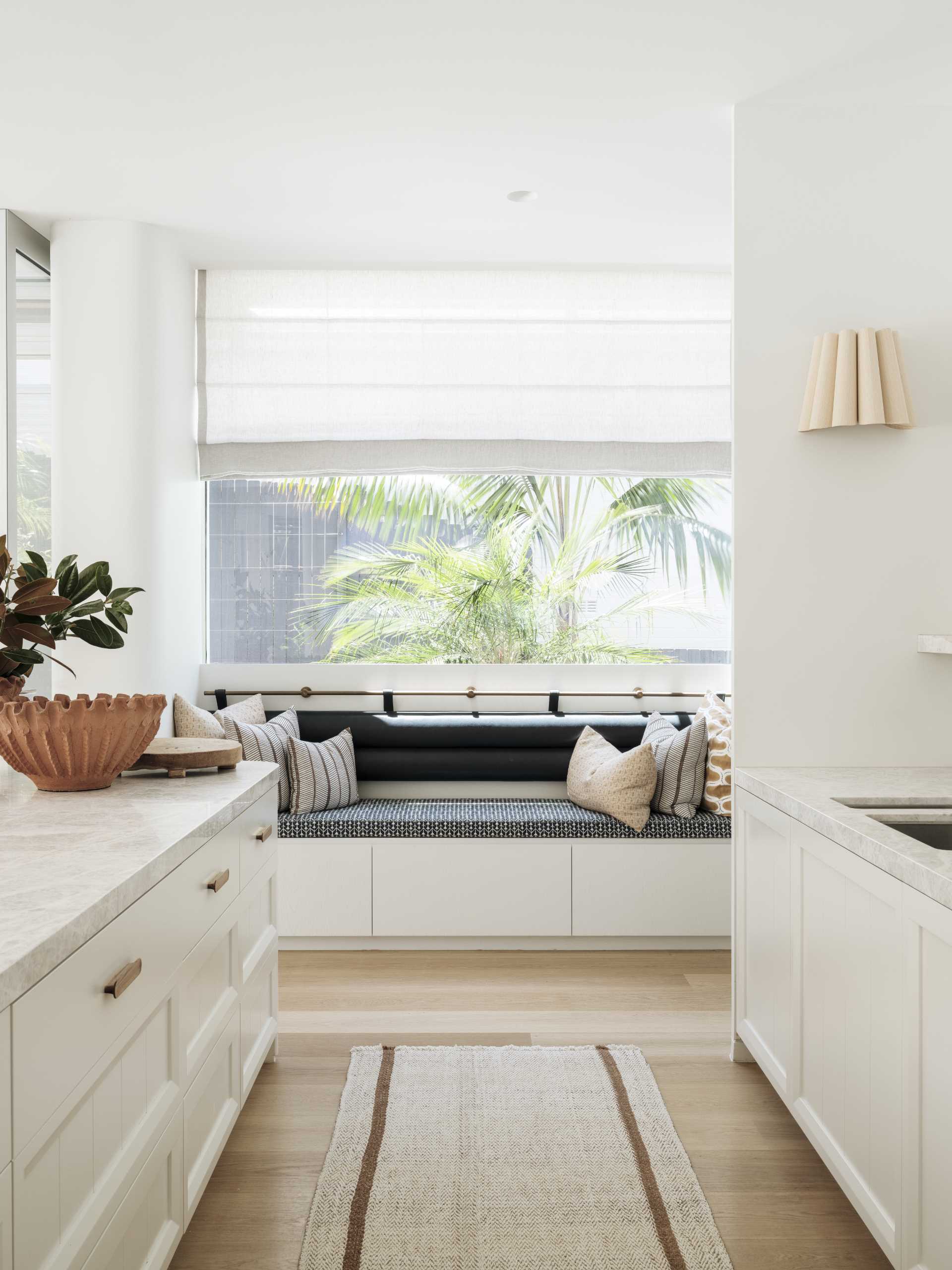 In this kitchen, white cabinets are complemented with a light countertop, while a bench has been placed underneath the nearby window.