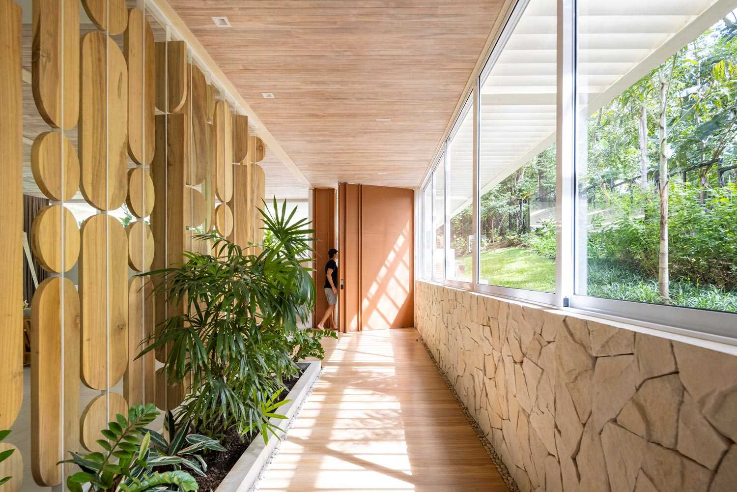 An oversized front door welcomes visitors to the home, while a small inside garden was placed at the entrance of the house giving it a touch of color that balances the light materials.