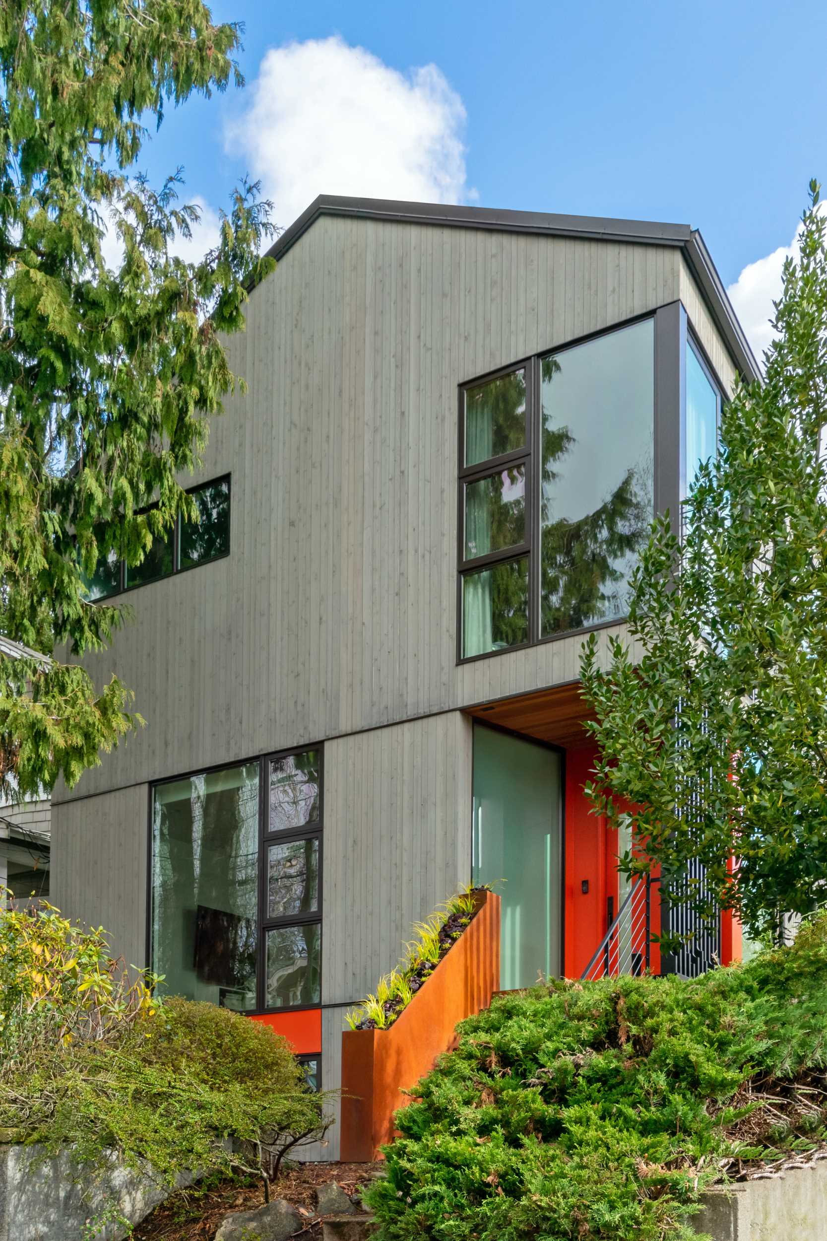 A modern house with a colorful front door, a steel planter, and a screen for added privacy.
