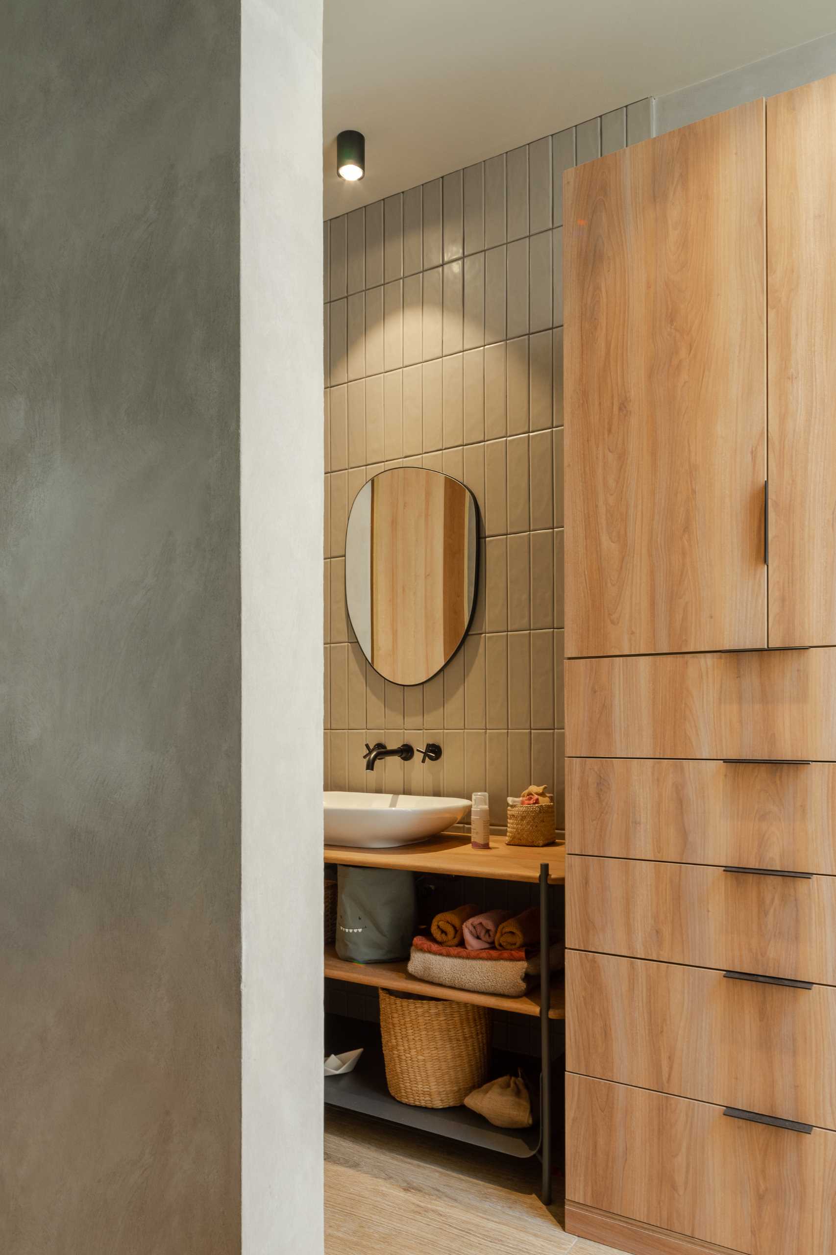 A modern bathroom with vertical green wall tiles, a white basin, and a wood vanity with open shelves.