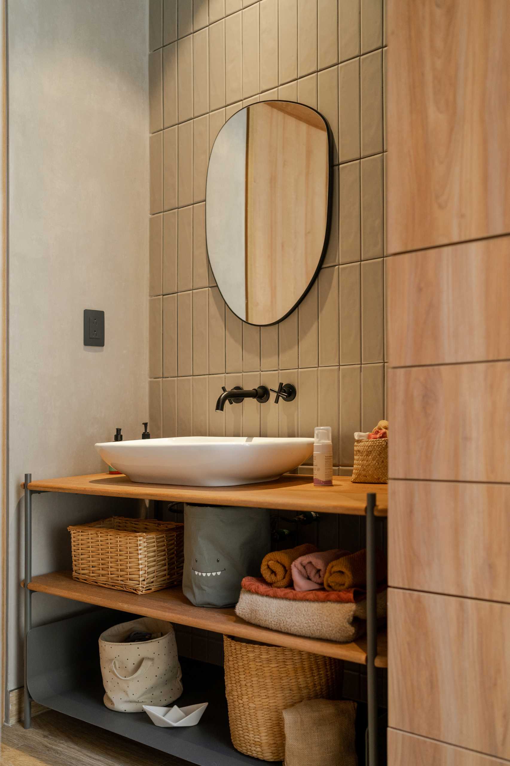 A modern bathroom with vertical green wall tiles, a white basin, and a wood vanity with open shelves.