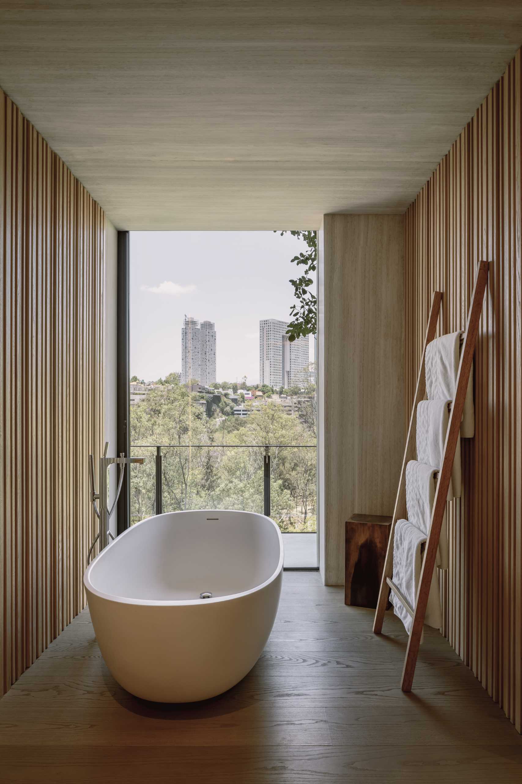 In this modern bathroom, a freestanding bathtub is positioned in front of the floor-to-ceiling window, providing relaxing views of the city.