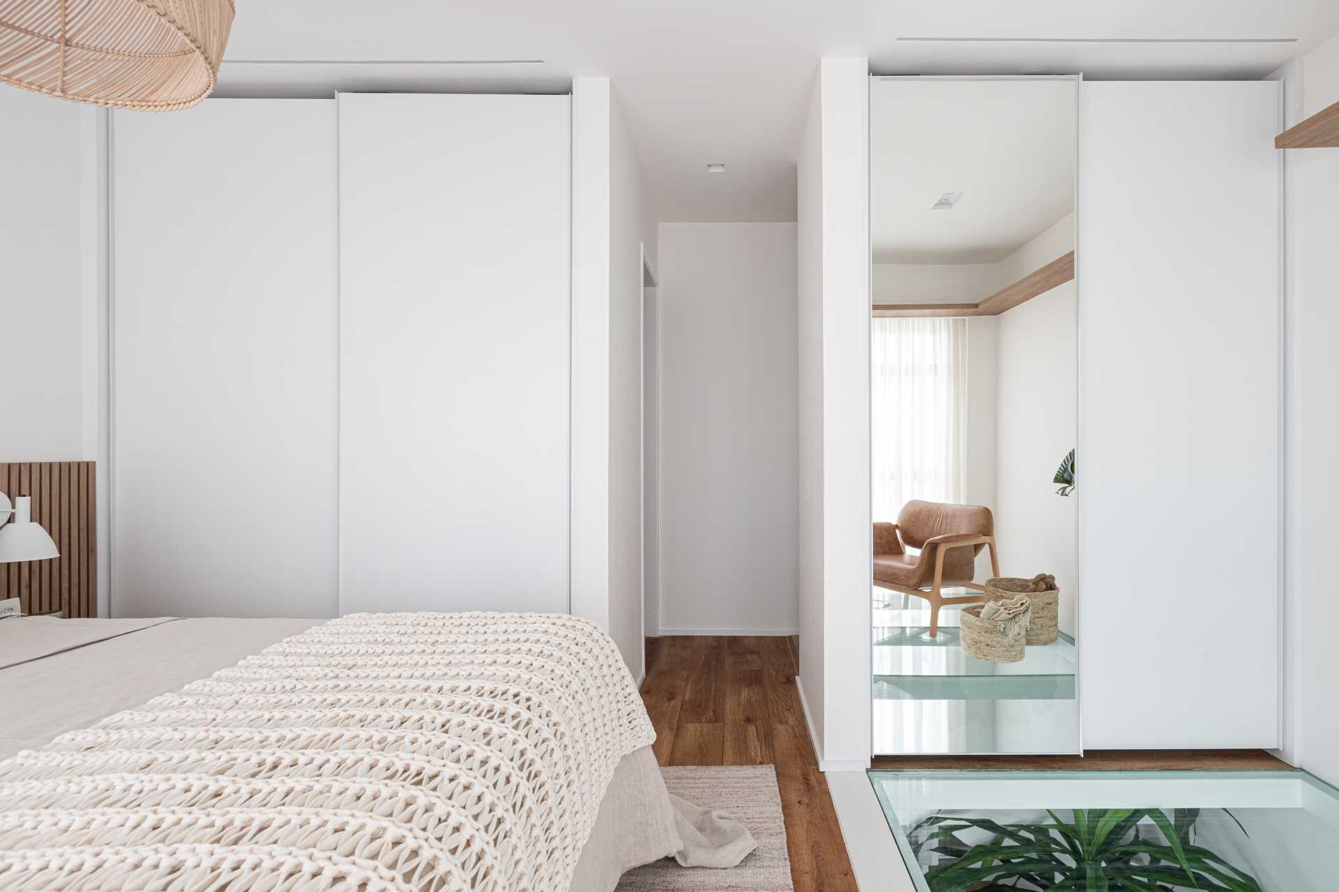 A modern bedroom with a partial glass floor that allows natural light to pass through to the living room below.