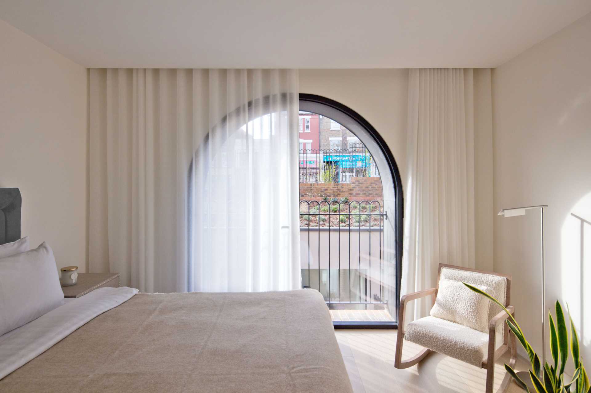 A modern bedroom with an arched window and floor-to-ceiling curtains.