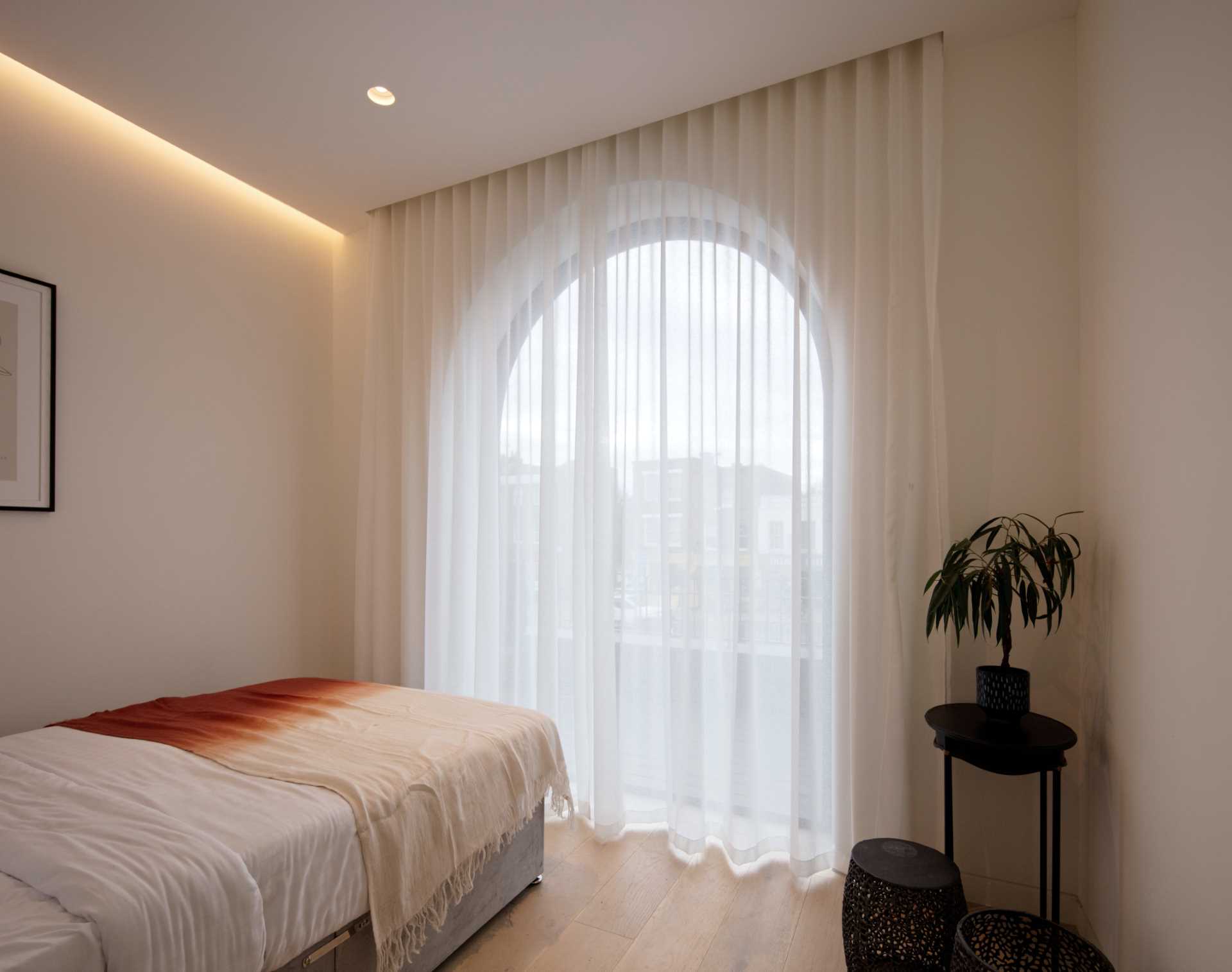 A modern bedroom with an arched window and floor-to-ceiling curtains.