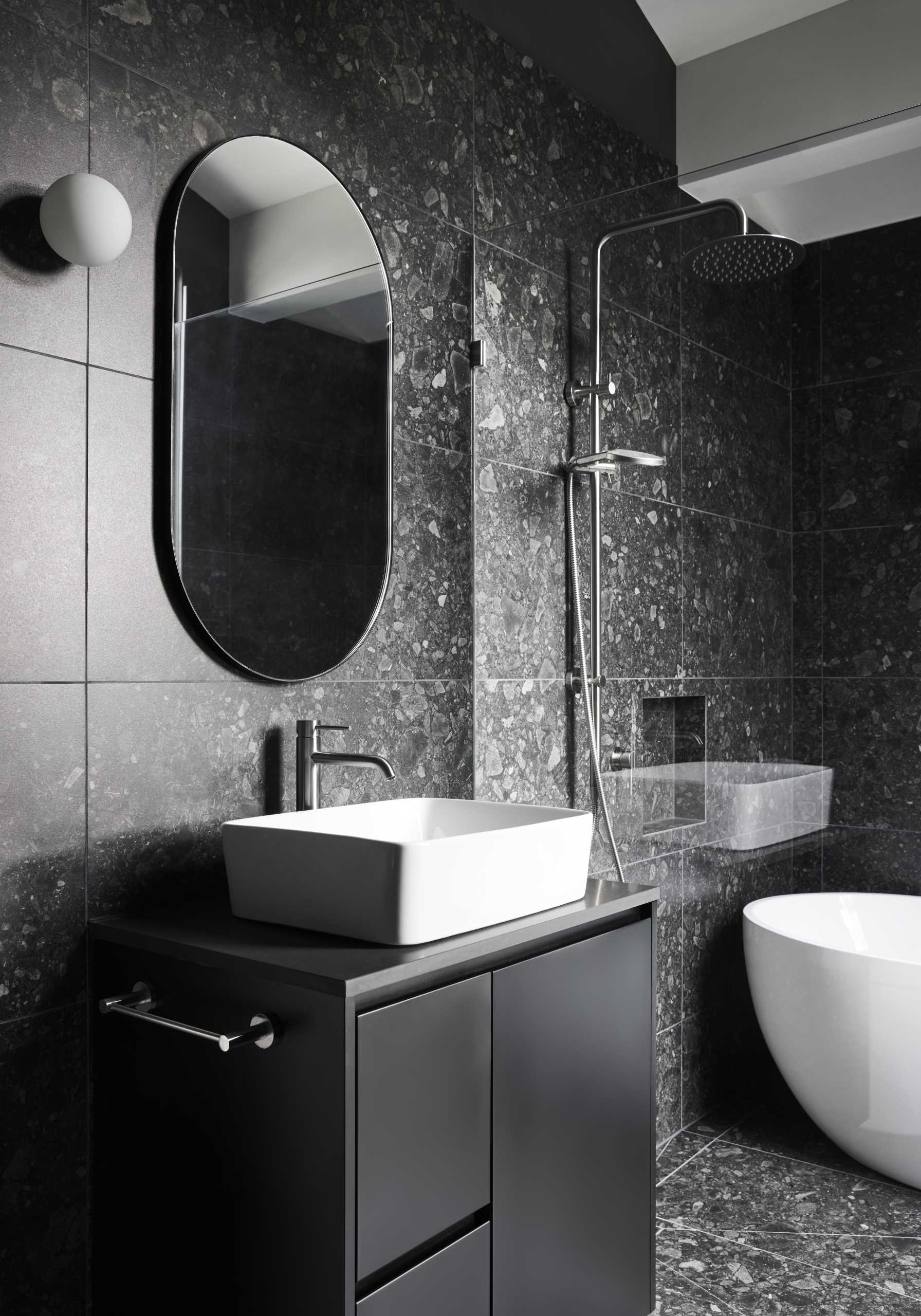 A modern black and grey bathroom with a white freestanding bathtub.