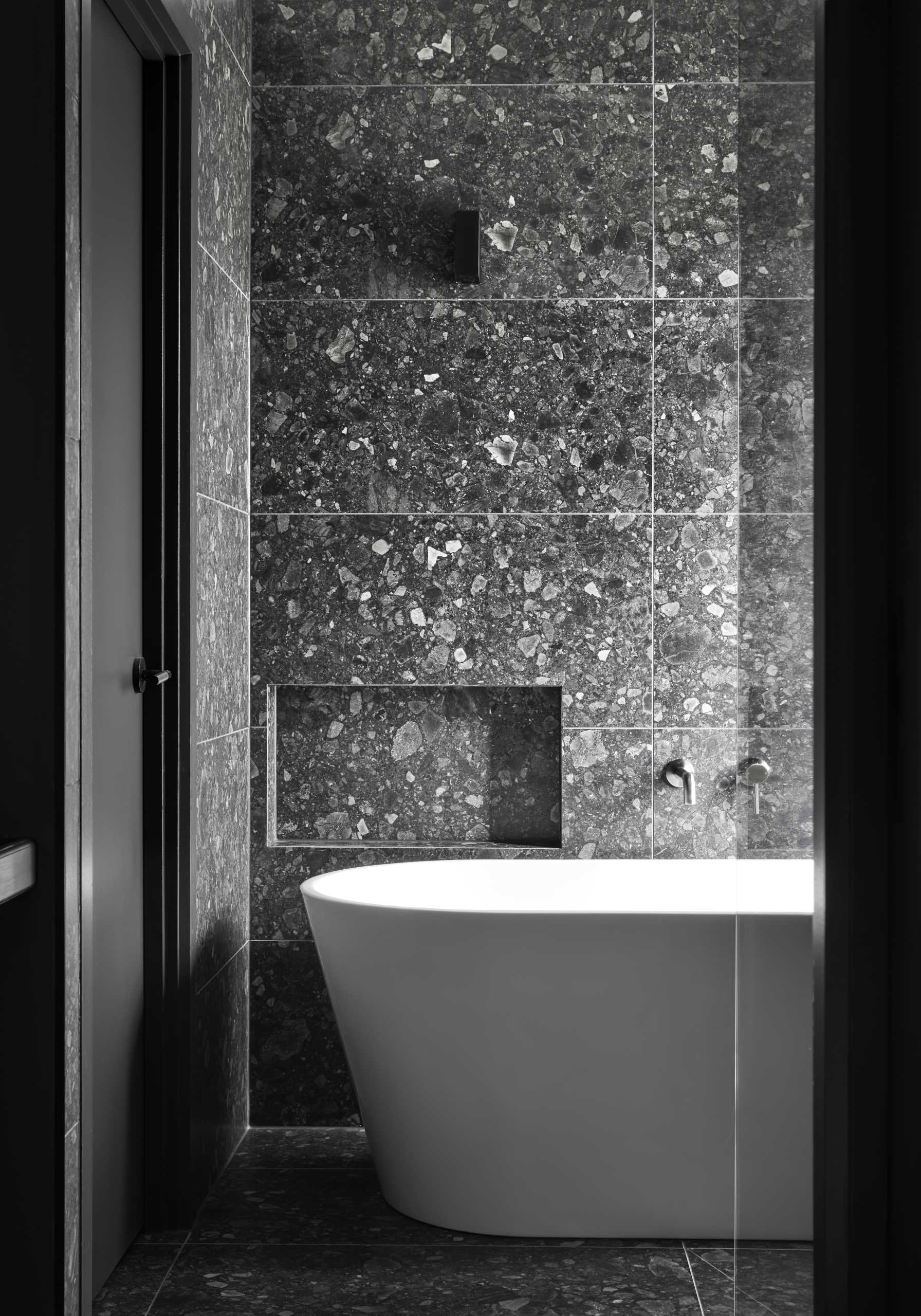 A modern black and grey bathroom with a white freestanding bathtub.