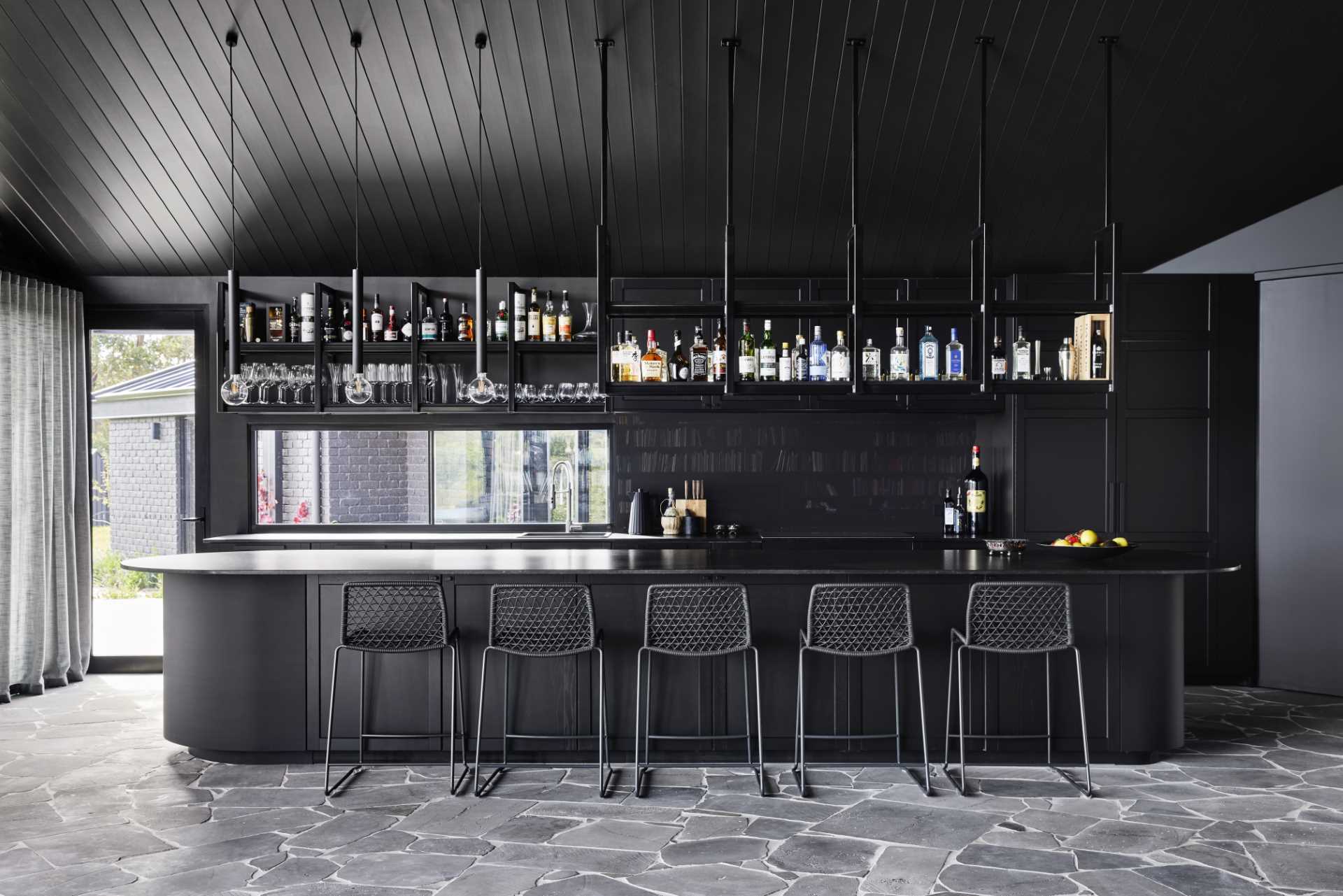 A modern black kitchen that's designed as a full-sized bar with a gentleman's club aesthetic.
