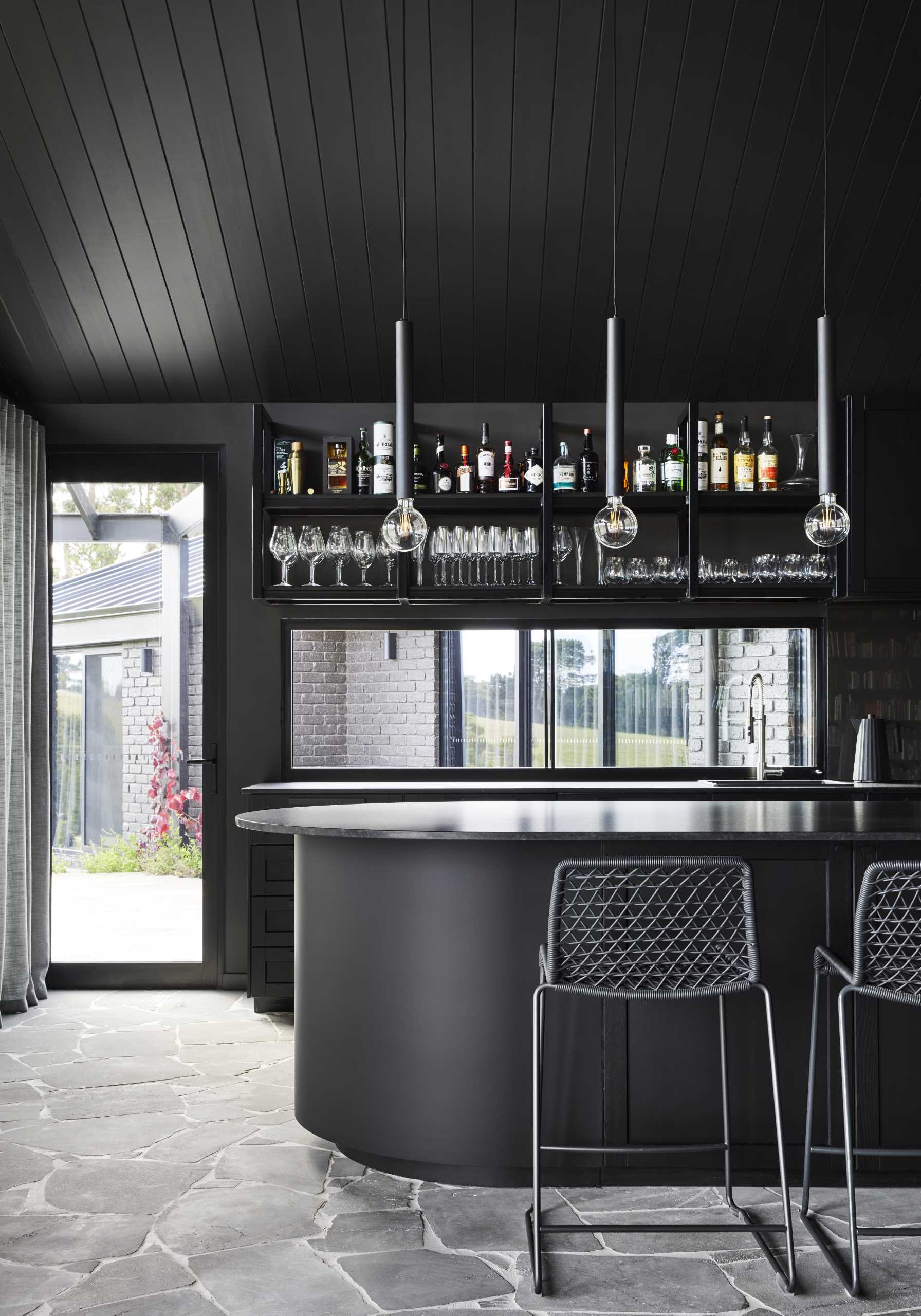 A modern black kitchen that's designed as a full-sized bar with a gentleman's club aesthetic.