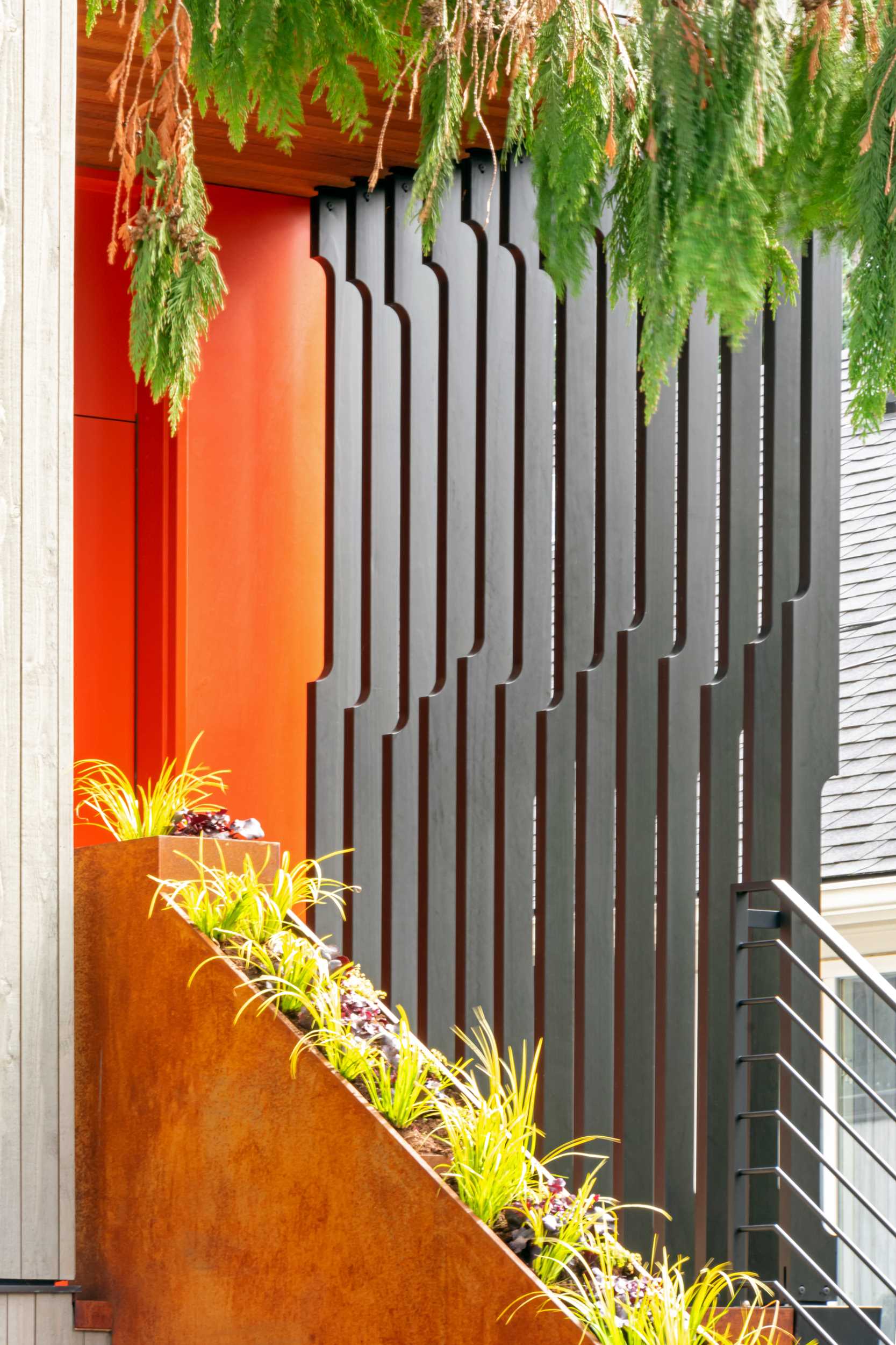 A modern house with a colorful front door, a steel planter, and a screen for added privacy.