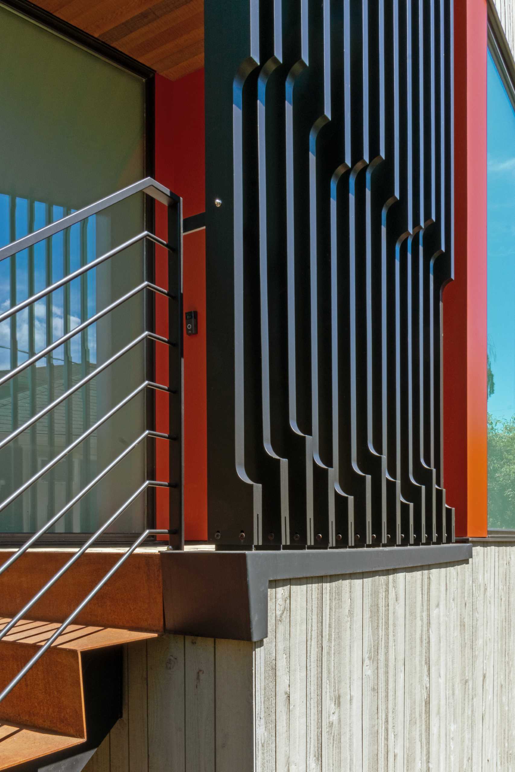 A modern house with a colorful front door, a steel planter, and a screen for added privacy.