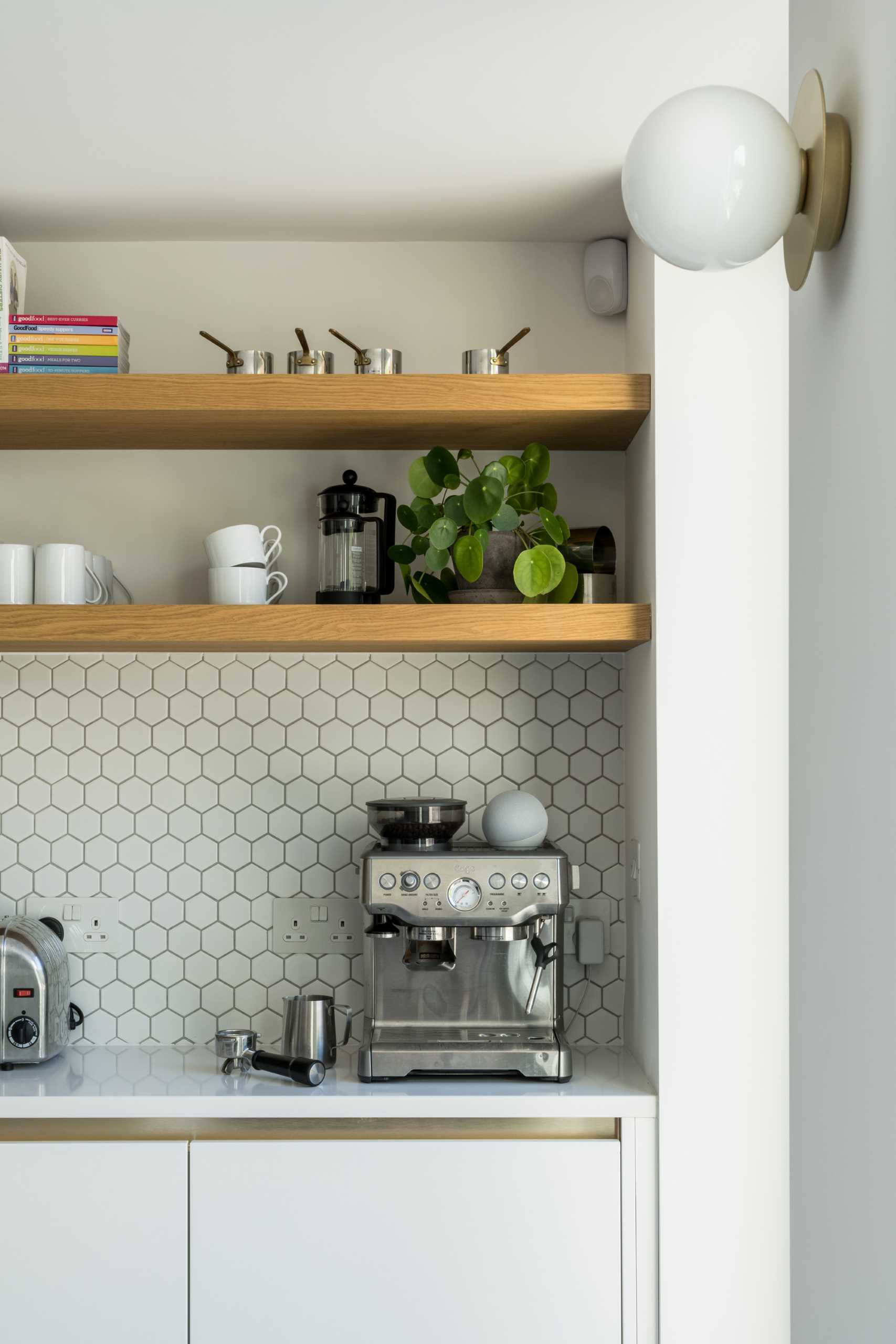 The new kitchen includes matte green cabinets, small hexagonal white tile backsplashes, wood shelves, and an island with undermount sink.