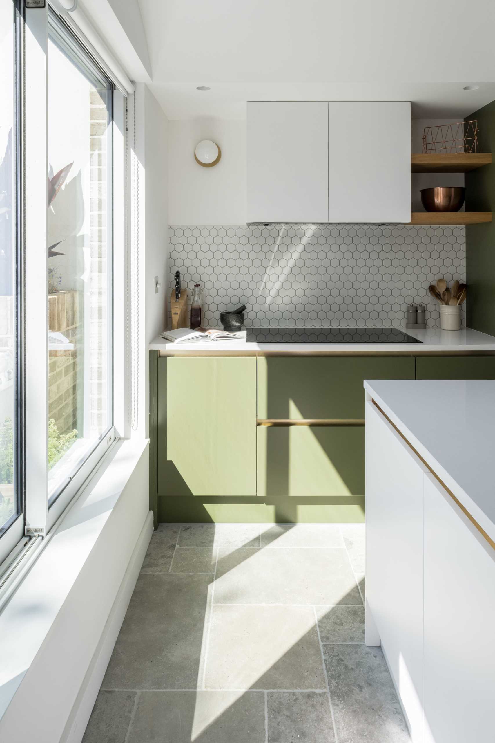 The new kitchen includes matte green and white cabinets, small hexagonal white tile backsplashes, wood shelves, and an island with undermount sink.
