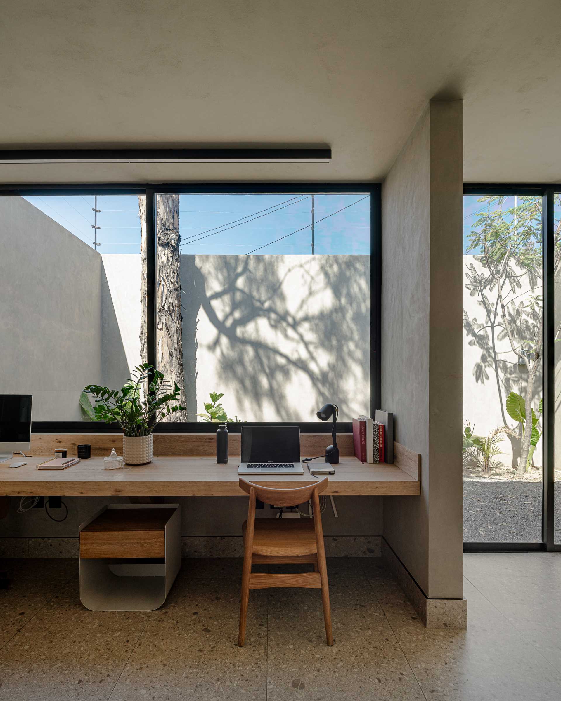 A home office with large windows is filled with natural light, and a wall-to-wall wood desk provides enough room for two people to work.