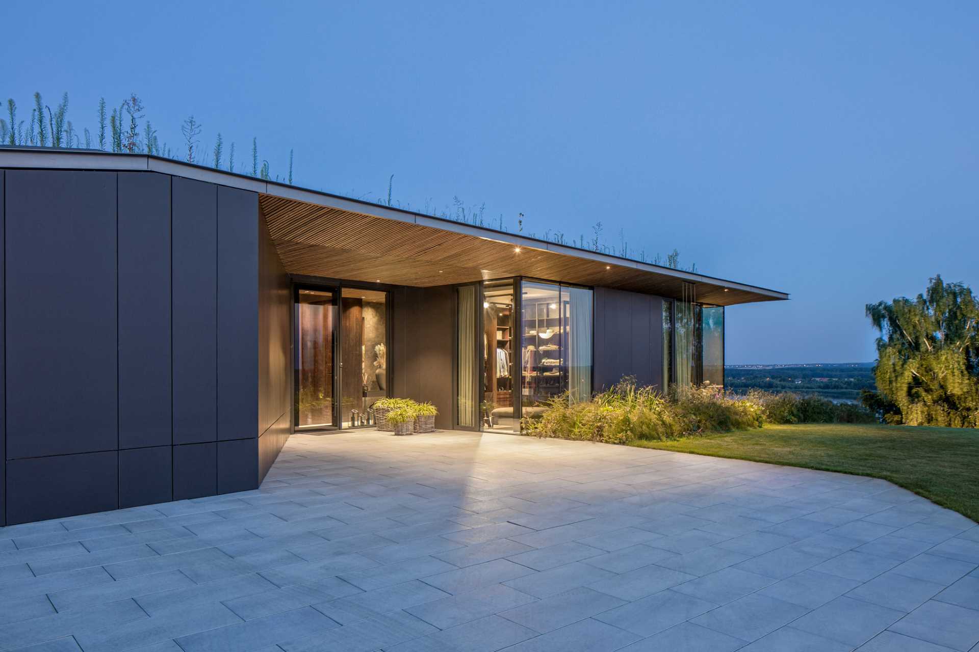 A paved area leads to the front door of this modern house with a green roof.