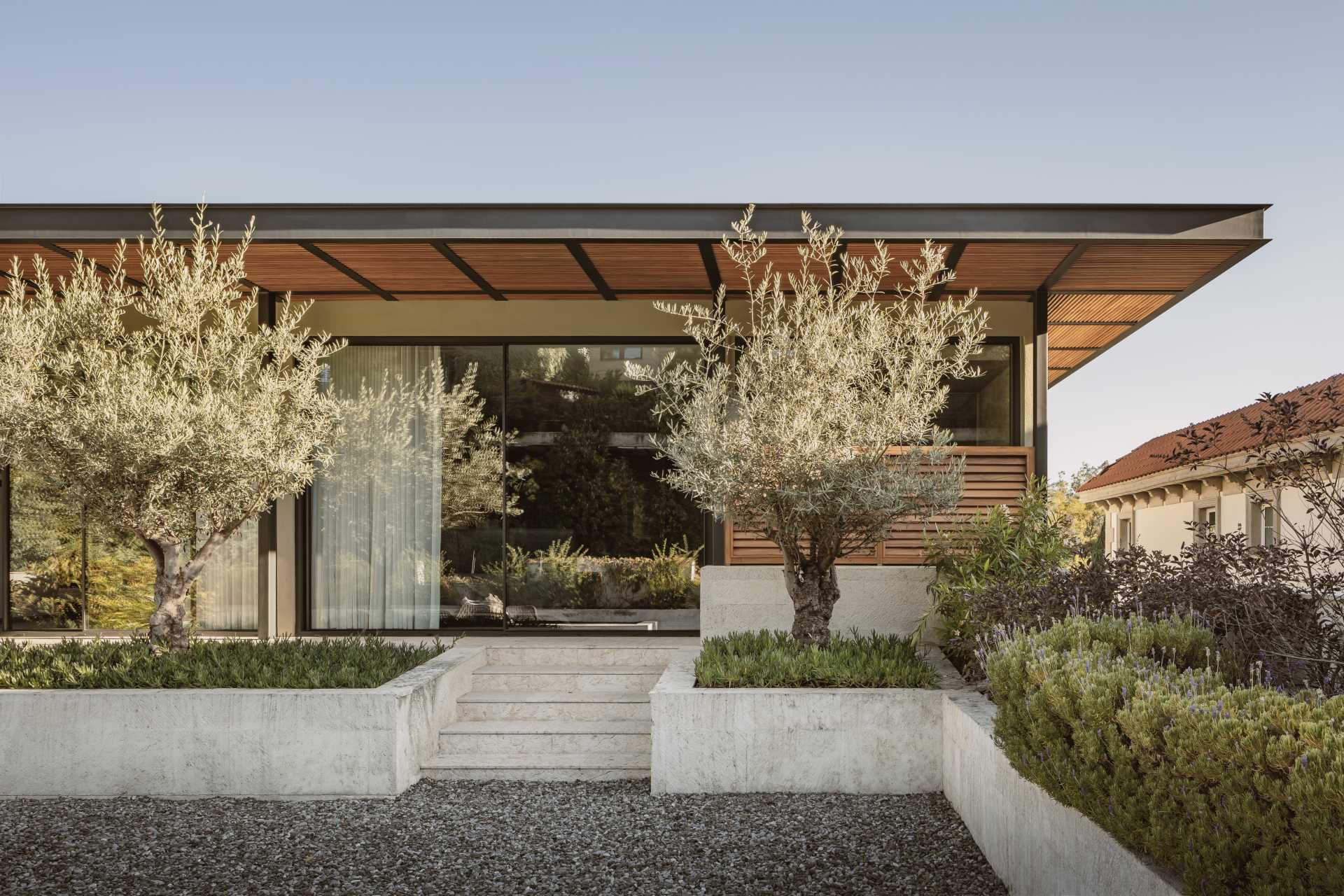 The exterior of this modern house features concrete, wood, and metal, as well as landscaped pathways and gardens.