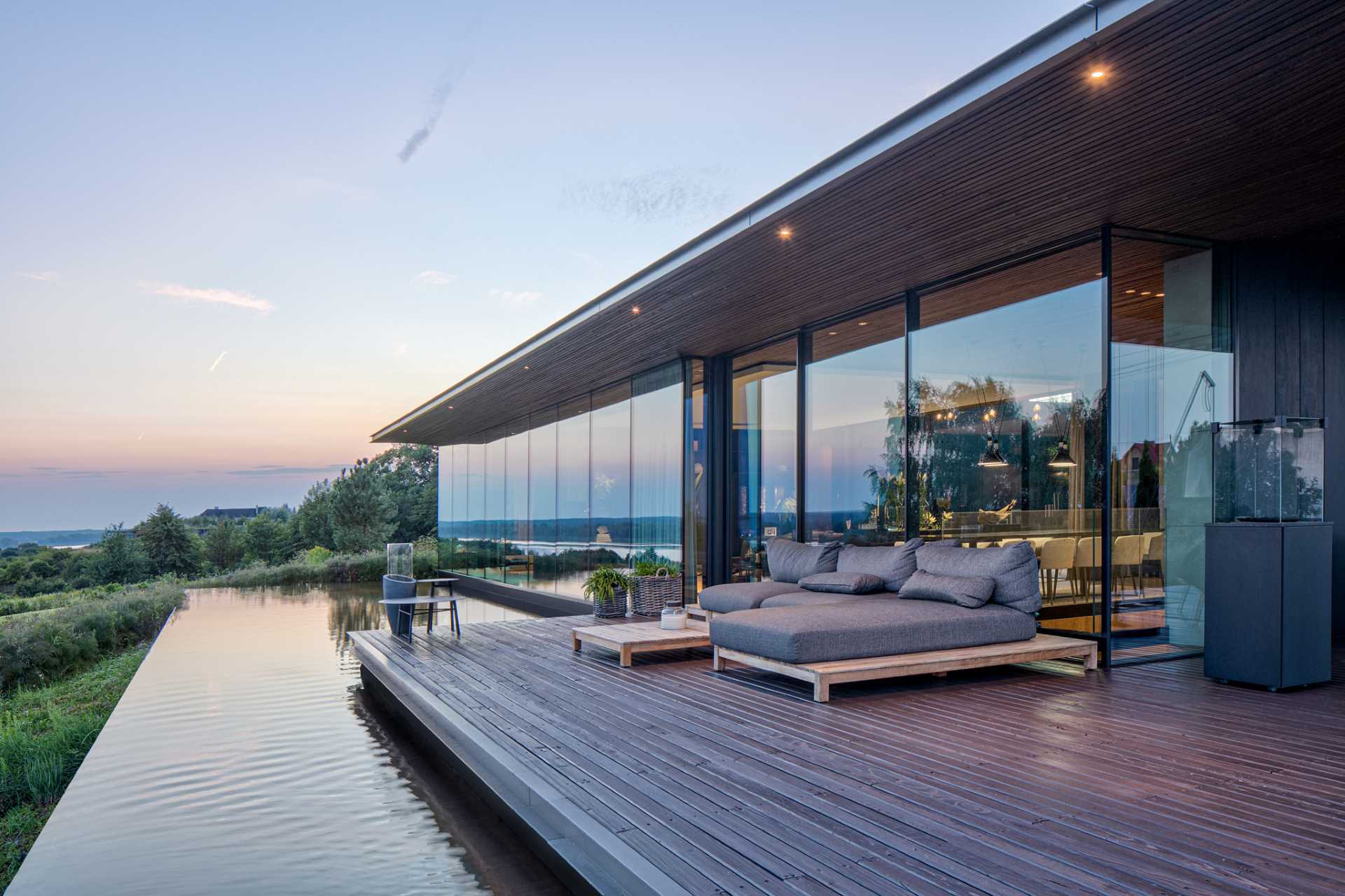 A modern home with a wall of windows, a deck, and a water feature.