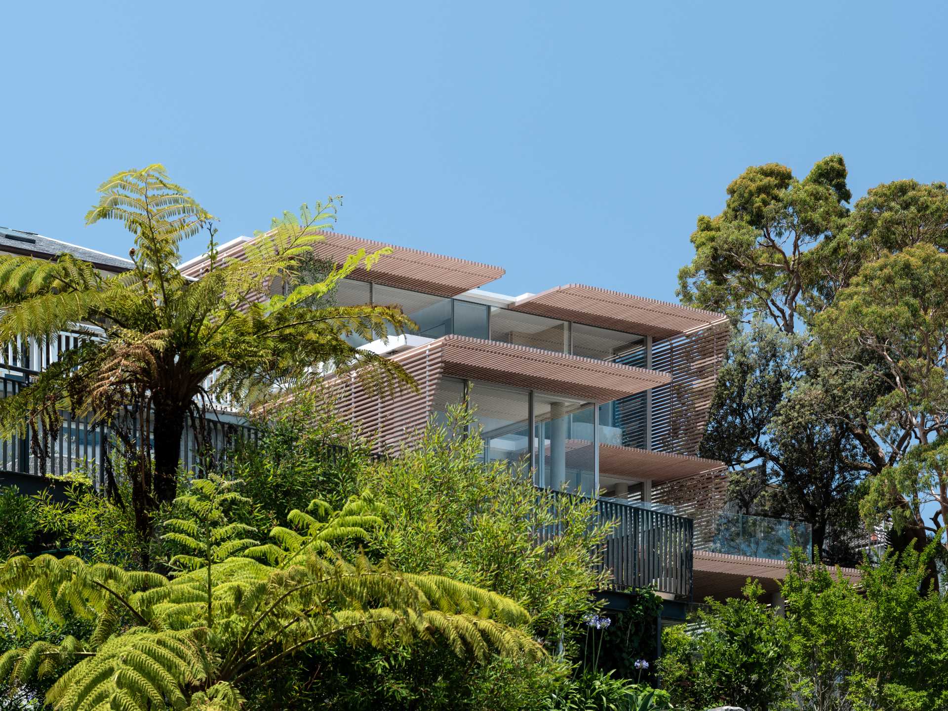 A modern home has wood-slat screens on its facade that create shading and privacy for the interior.