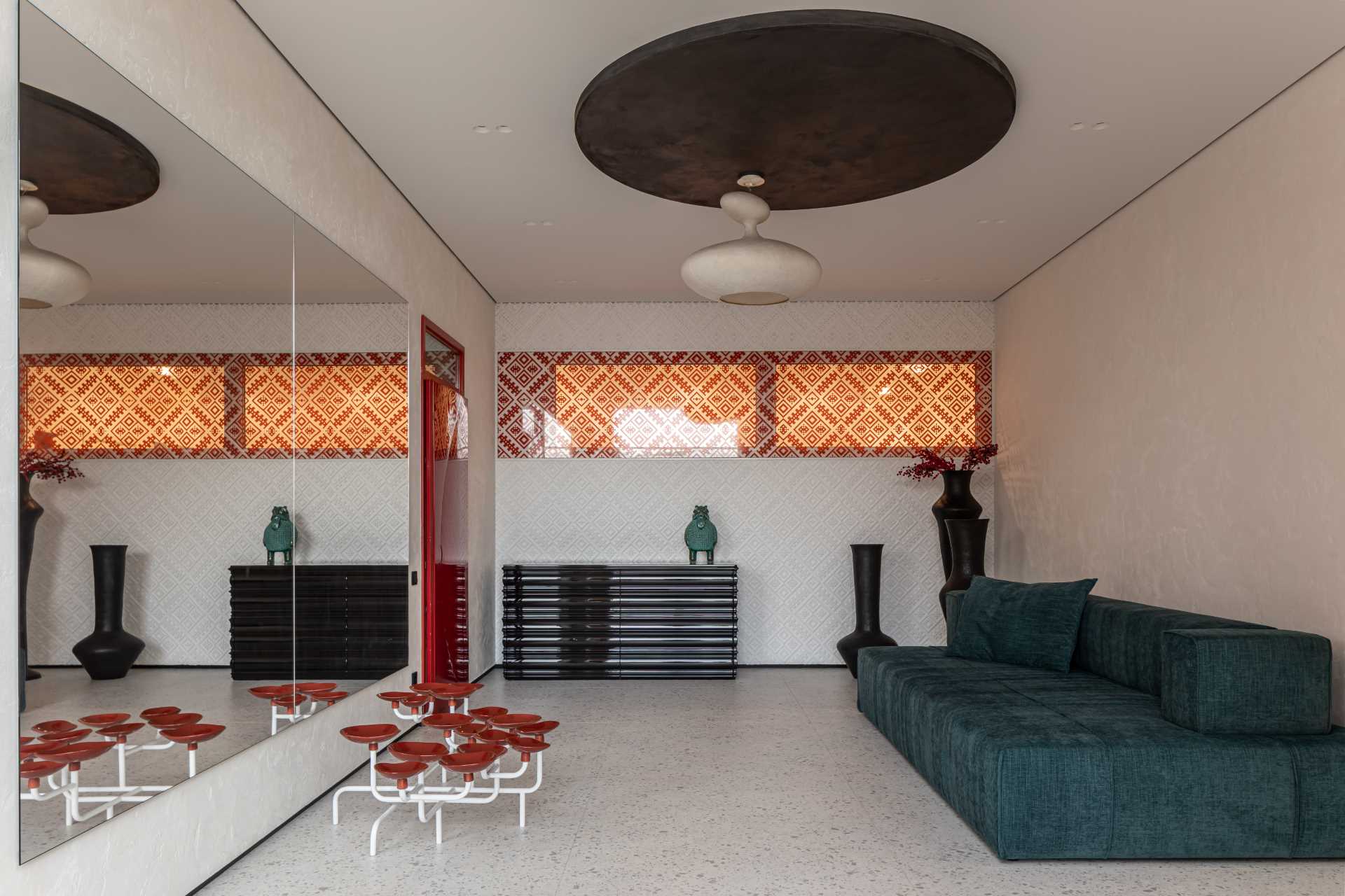 A delicate pattern on the wall transitions from white to red, while a large mirror reflects the turquoise couch.