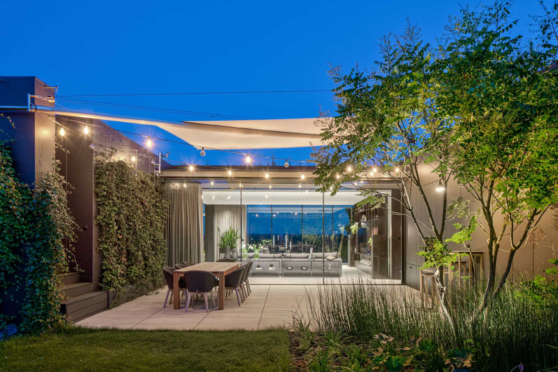 A modern house with an outdoor dining area that's lit with string lights.