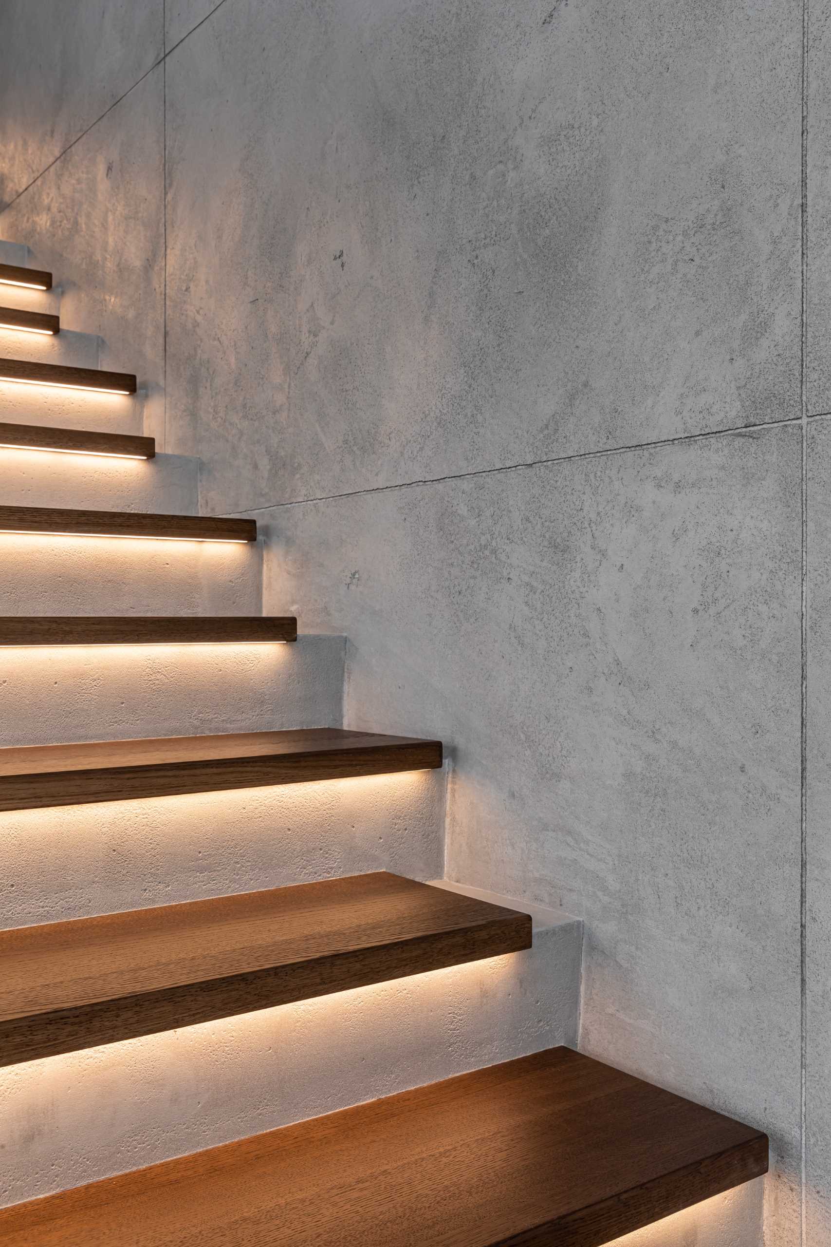 A modern home with concrete and wood stairs, that also include hidden lighting underneath the treads