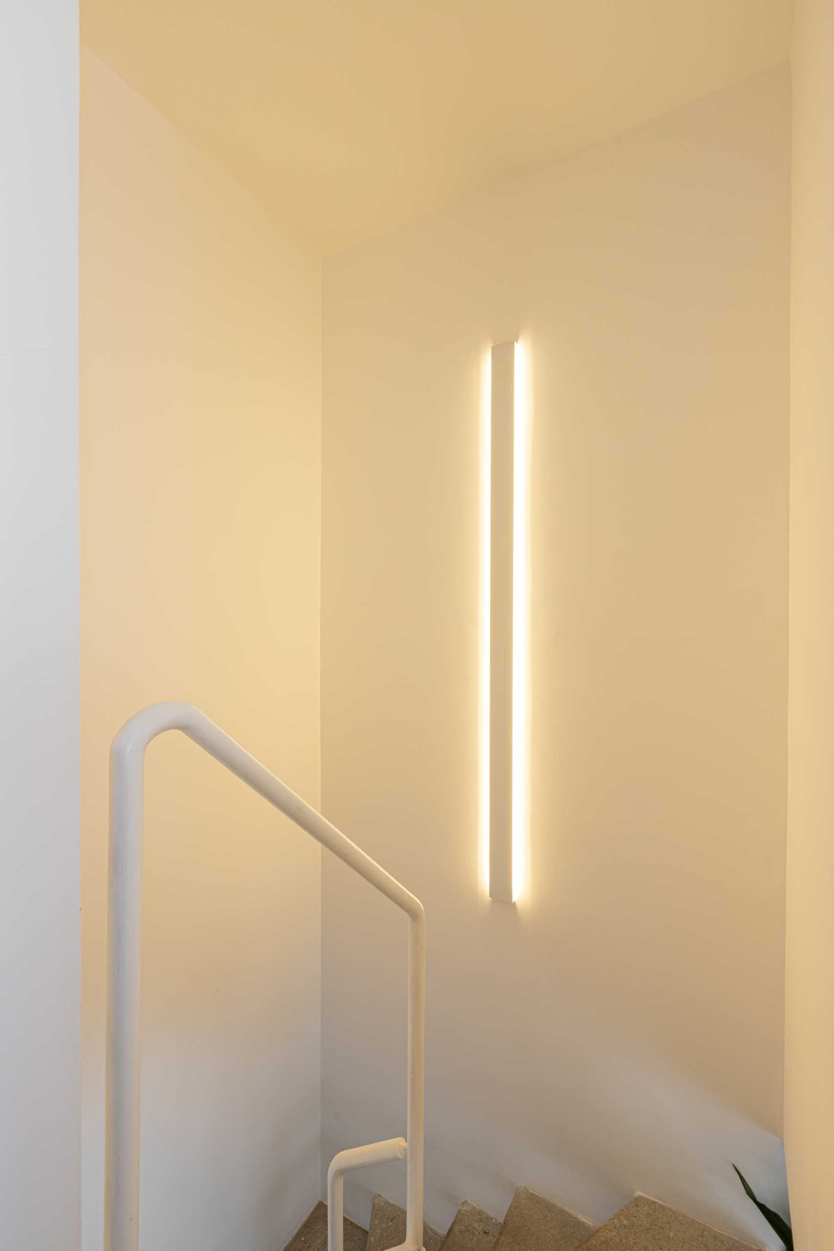 A modern staircase with a vertical wall light.