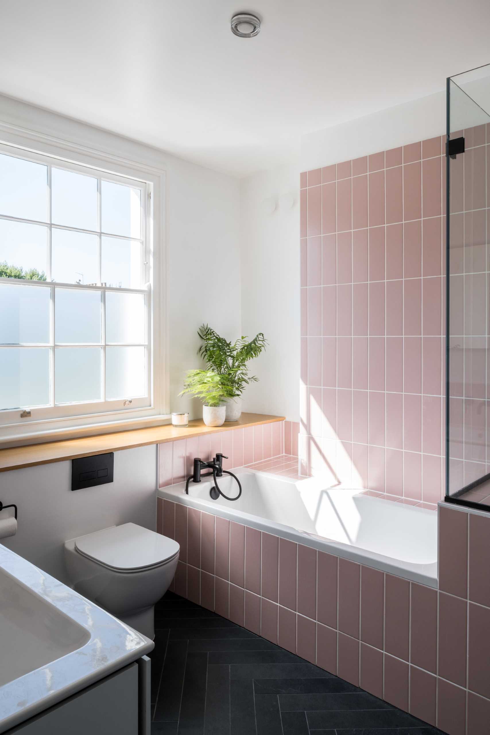 In this bathroom, pink subway tiles in a vertical layout cover the shower wall and the bathtub surround.