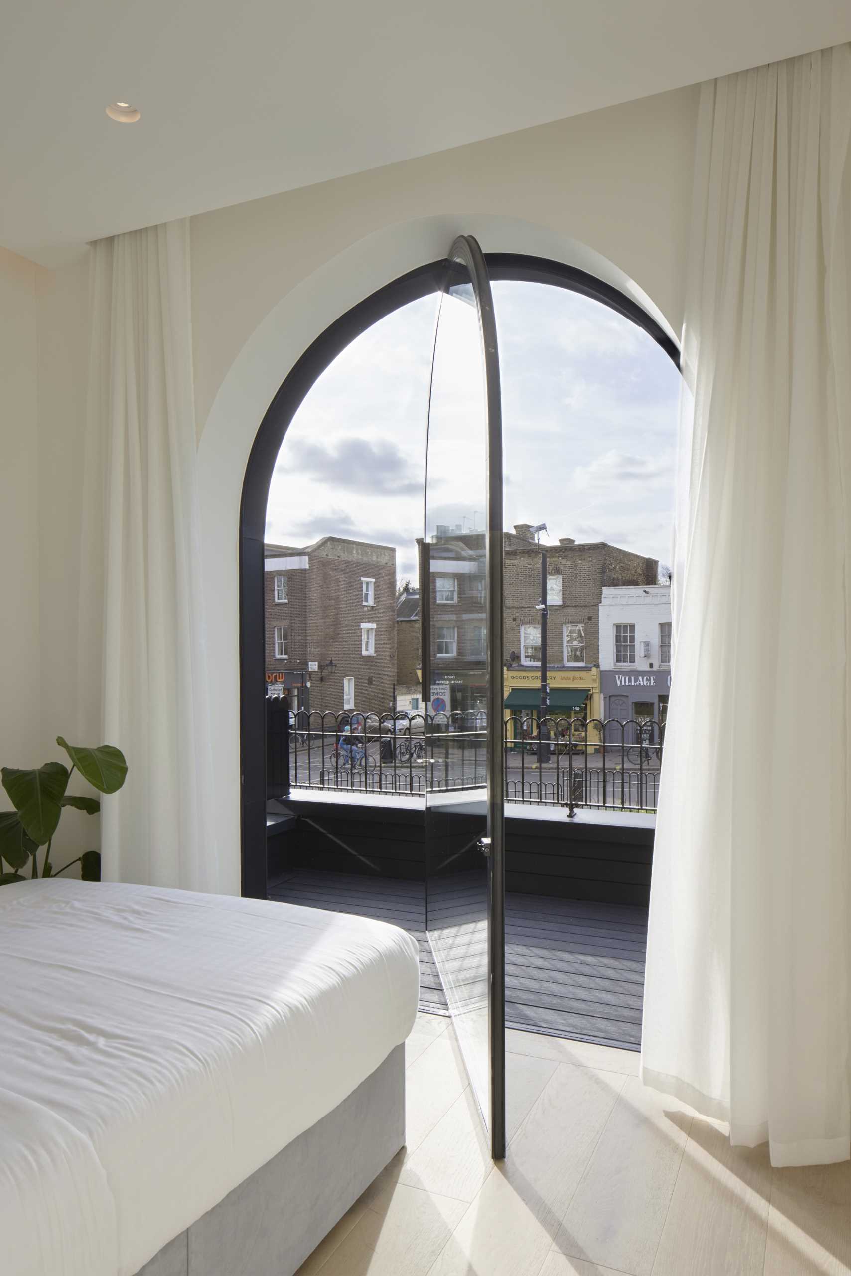 A modern bedroom with a pivoting arched window and floor-to-ceiling curtains.