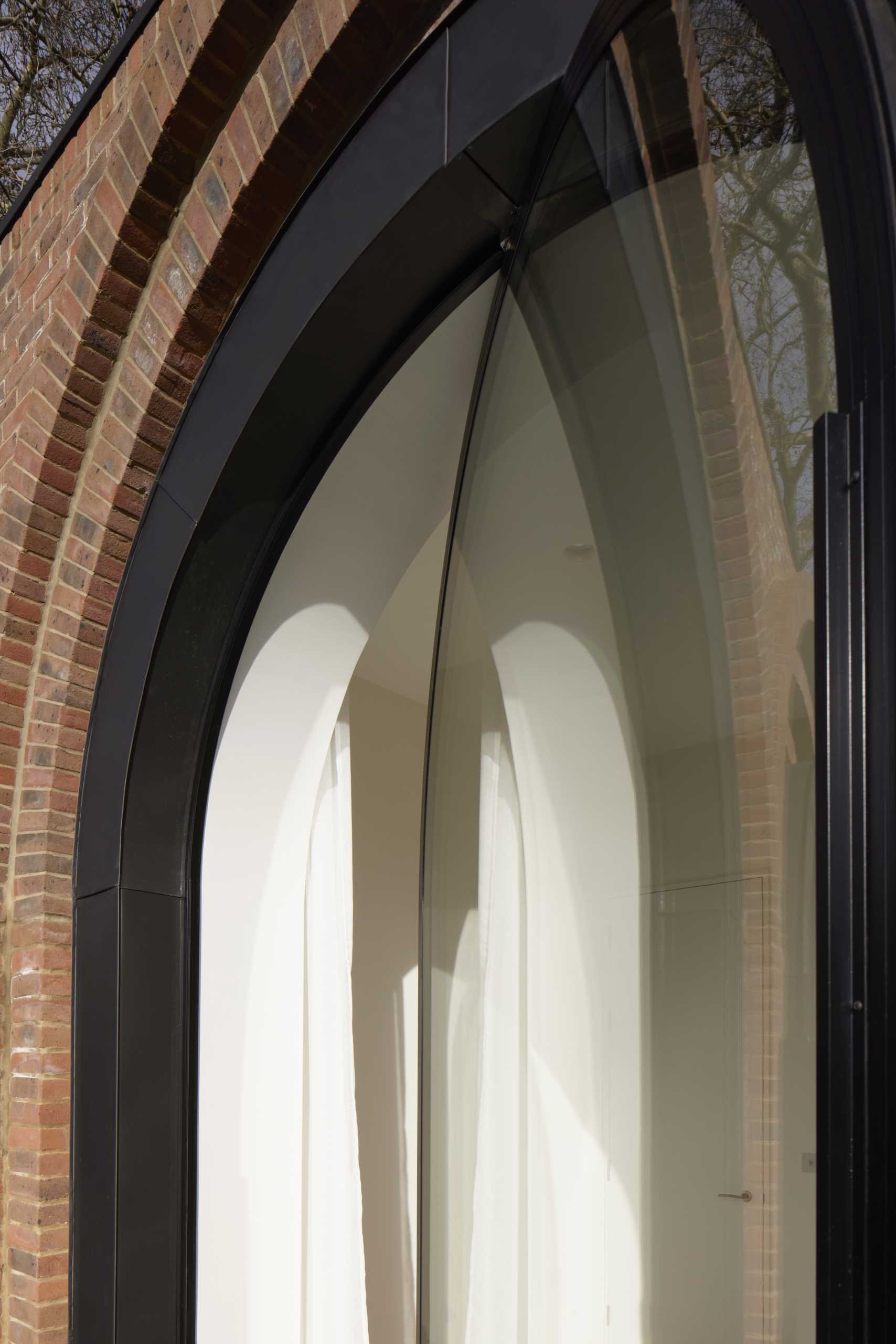 A modern bedroom with a pivoting arched window with black frames.