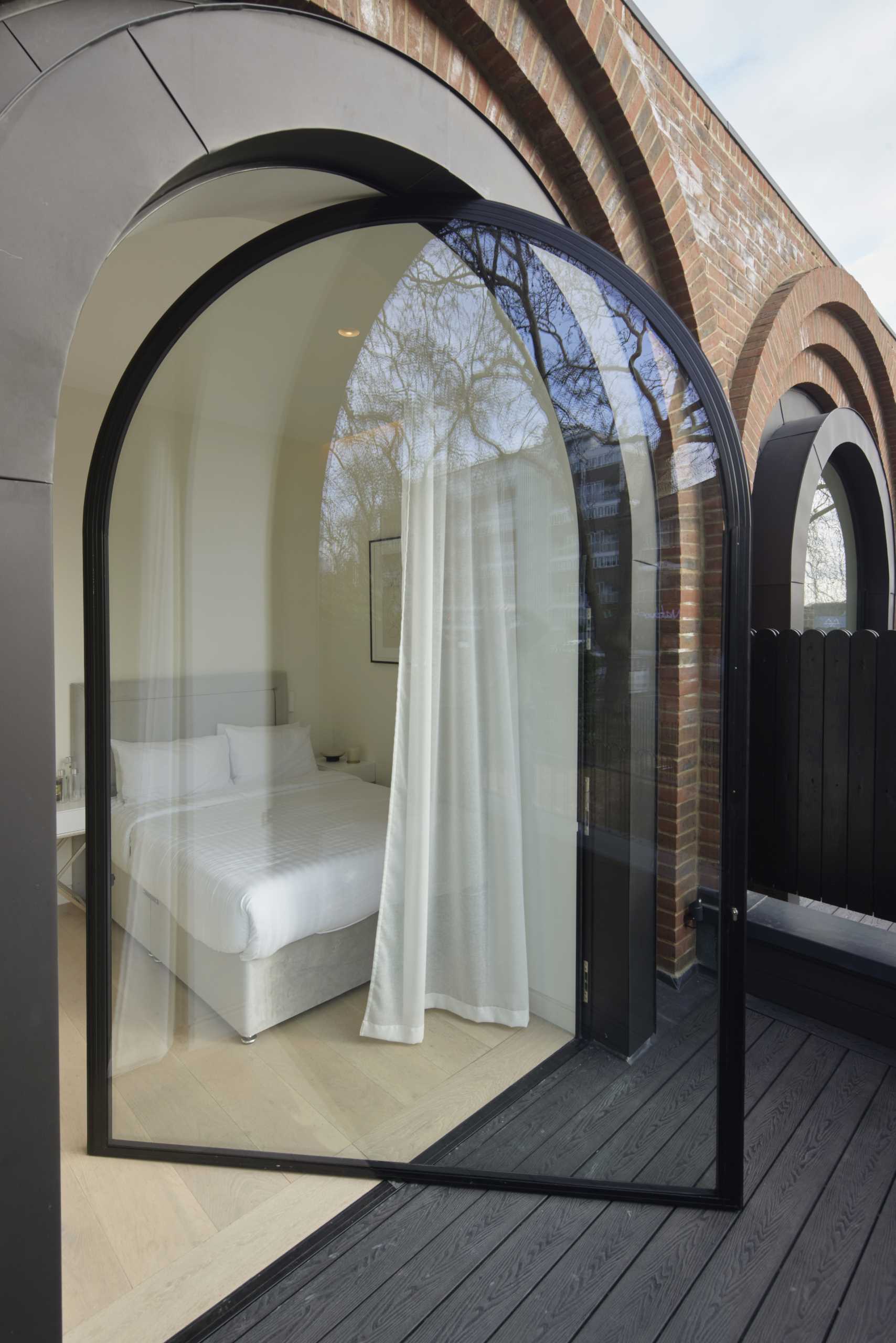 A modern bedroom with a pivoting arched window with black frame.
