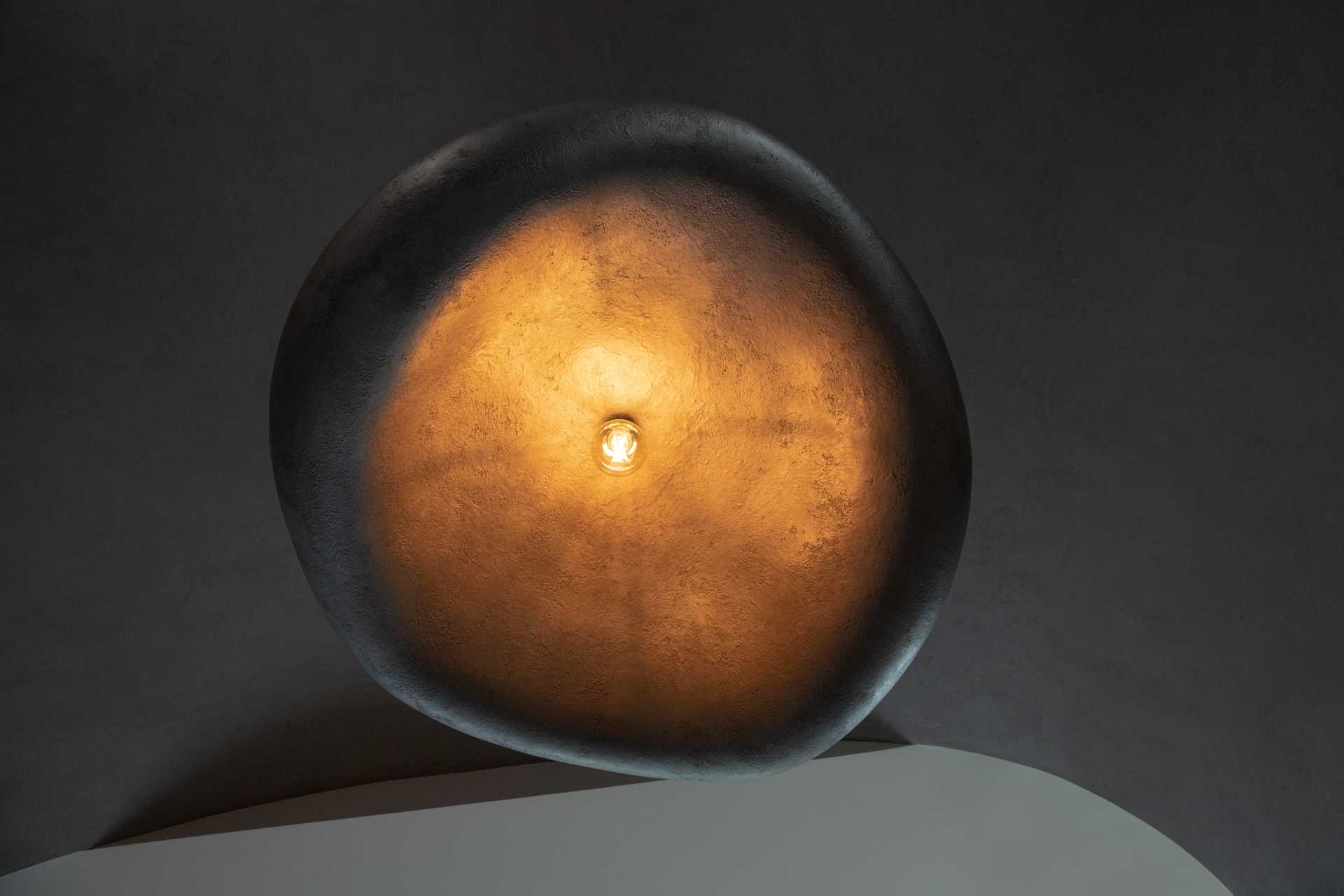 A large sculptural pendant light with a gray exterior, that reflects the light and offers a warm glow.
