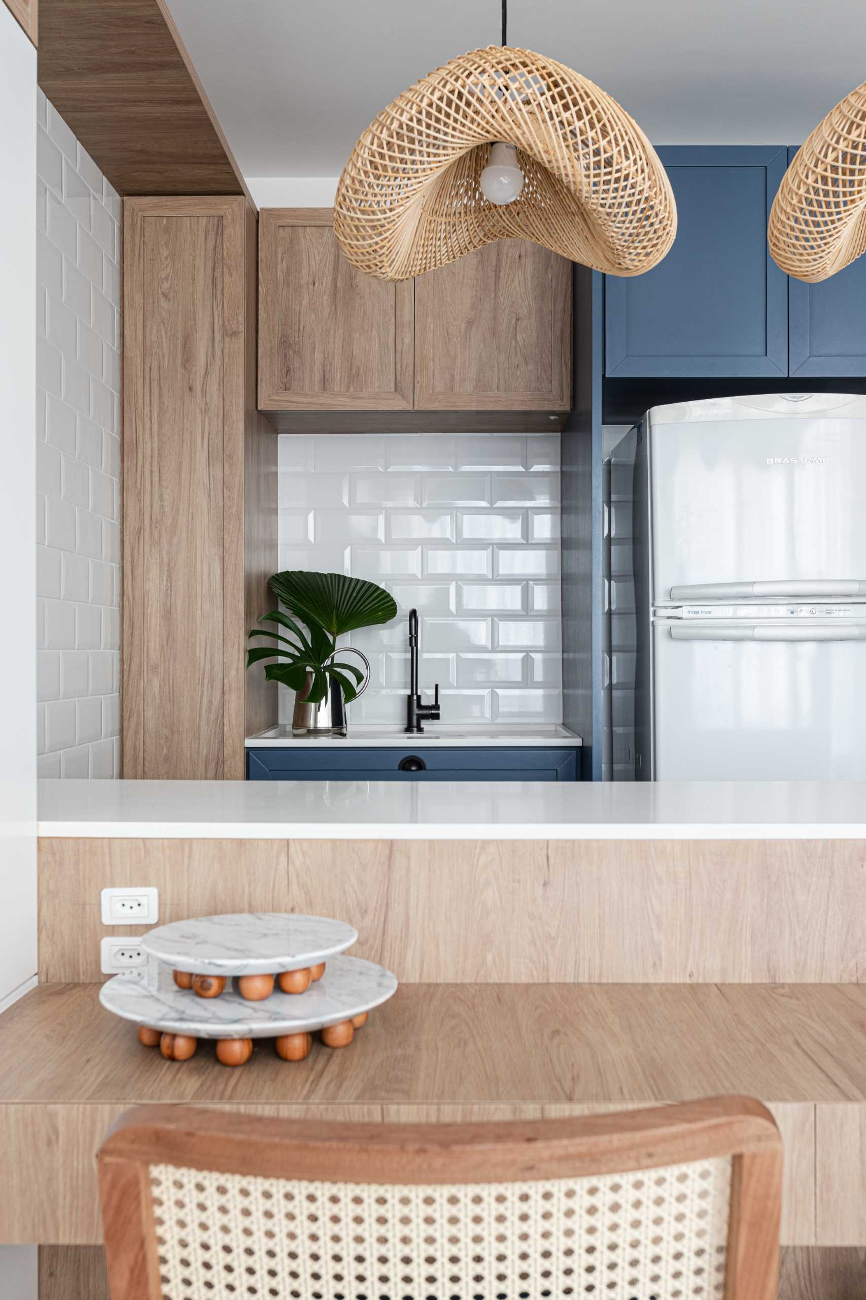 This small kitchen features wood and blue cabinets, white subway tile, and a pair of woven pendant lights.