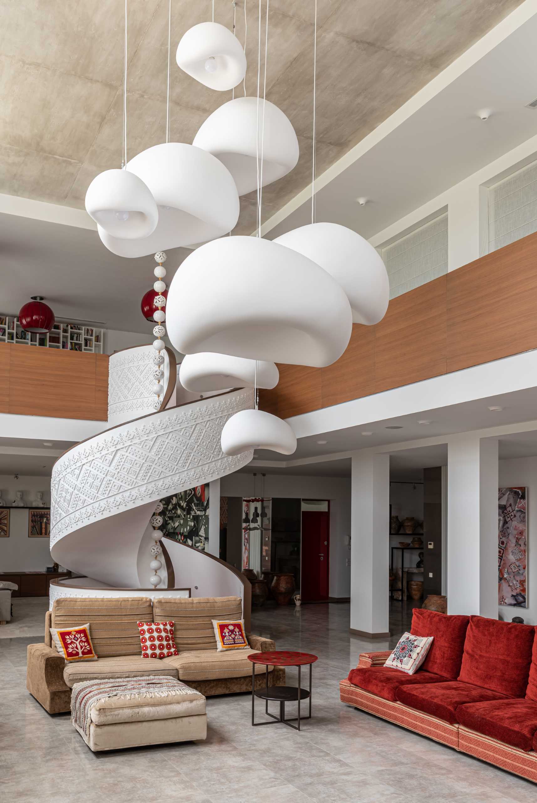 A living room with a white spiral staircase with a delicate pattern on its exterior and wood handrails, also includes sculptural pendant lights.