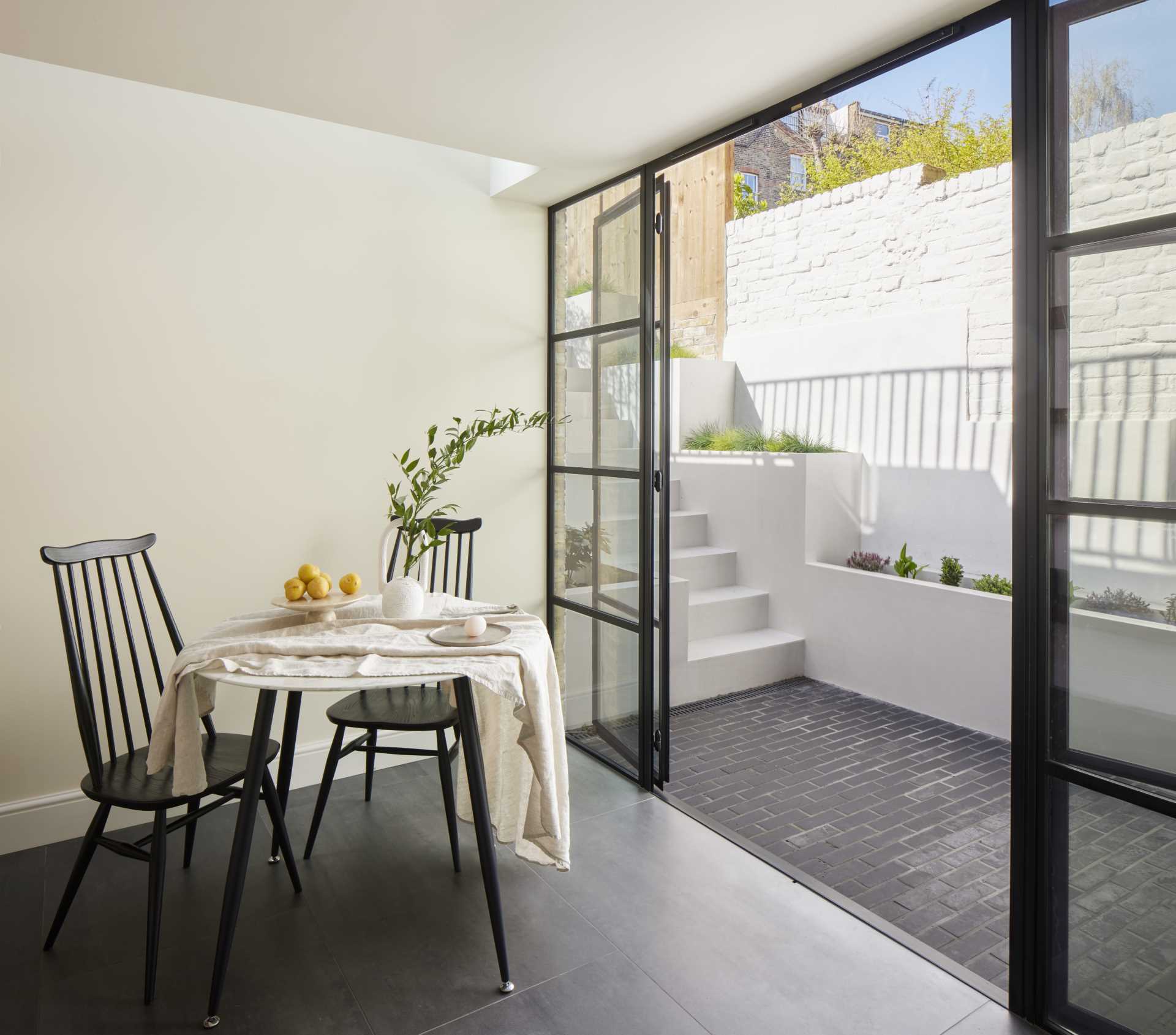 Black framed glass doors connect the patio with a breakfast room, which has been finished with dark floor tiles and light walls.