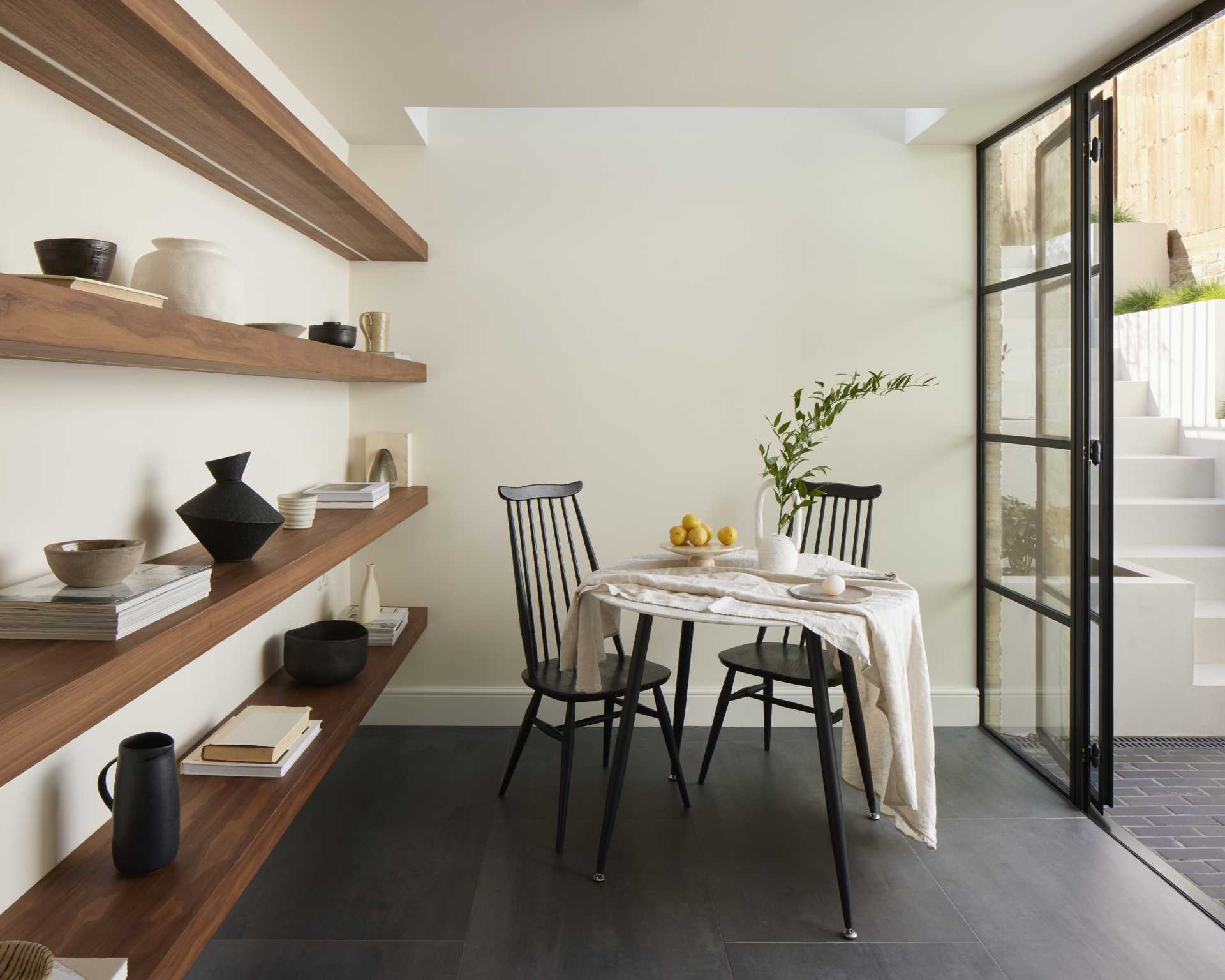 Black framed glass doors connect the patio with a breakfast room, which has been finished with dark floor tiles and light walls.