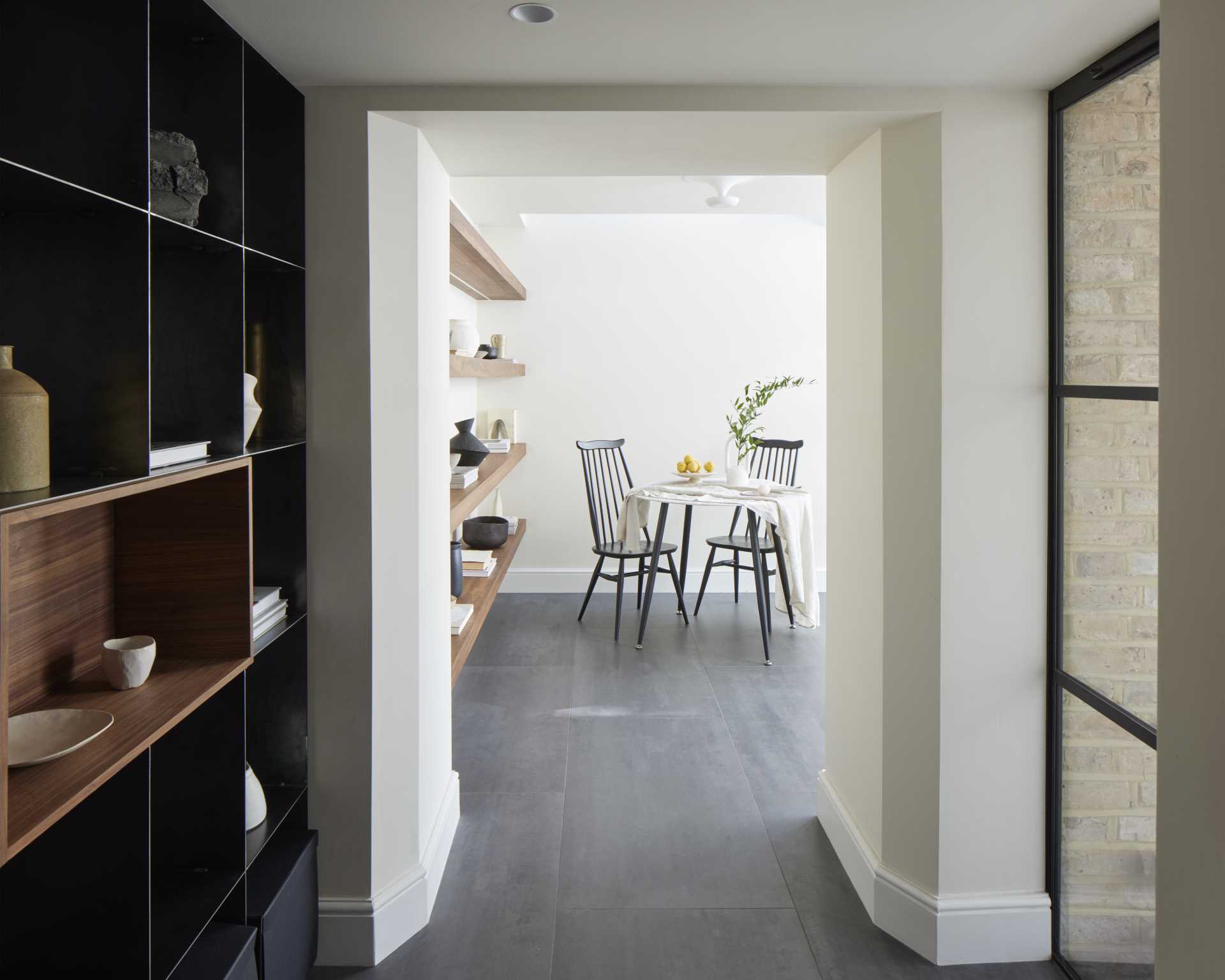 This breakfast room includes floating wood shelves, and in the adjacent hallway, there's a metal shelving unit with a dark wood niche.