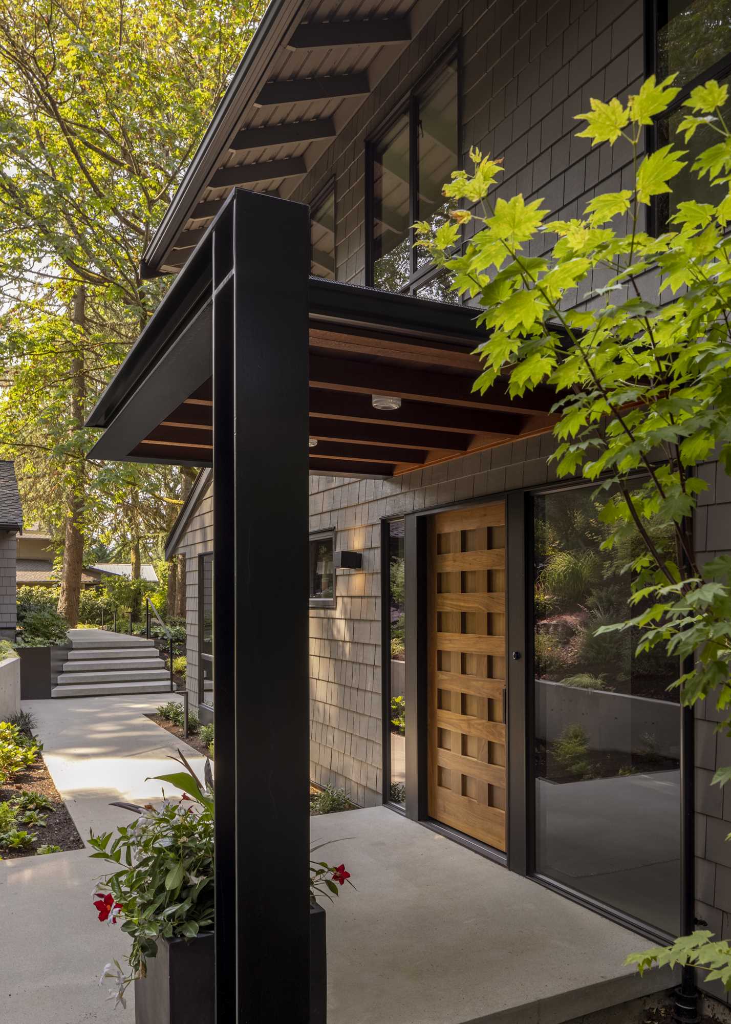 A steel and wood canopy provides lighting and protection from the rain, while thoughtfully placed landscaping areas buffer the home and offer privacy to the spaces inside.