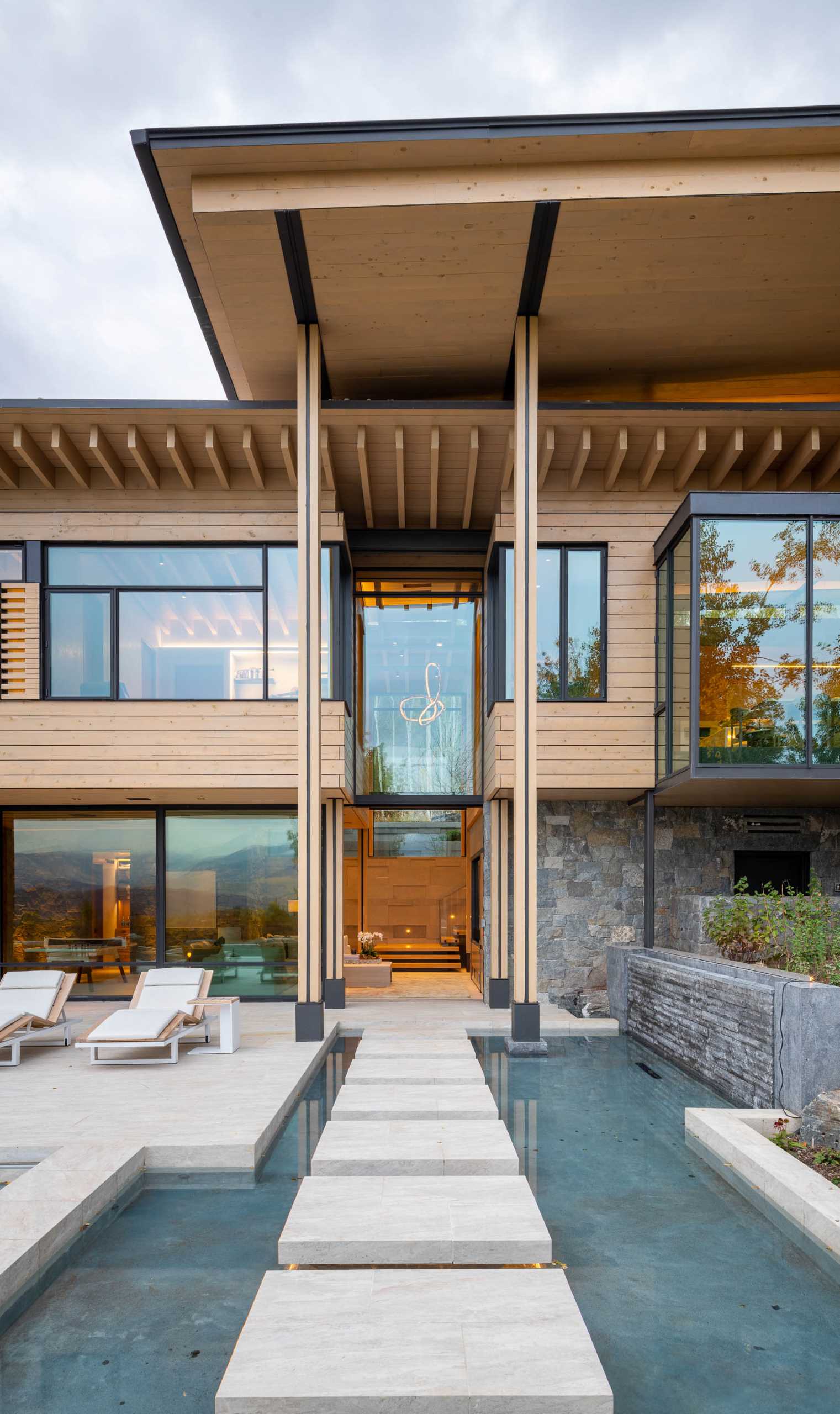 A contemporary mountain home clad in stone, wood, steel, and glass, also has a swimming pool and water feature.