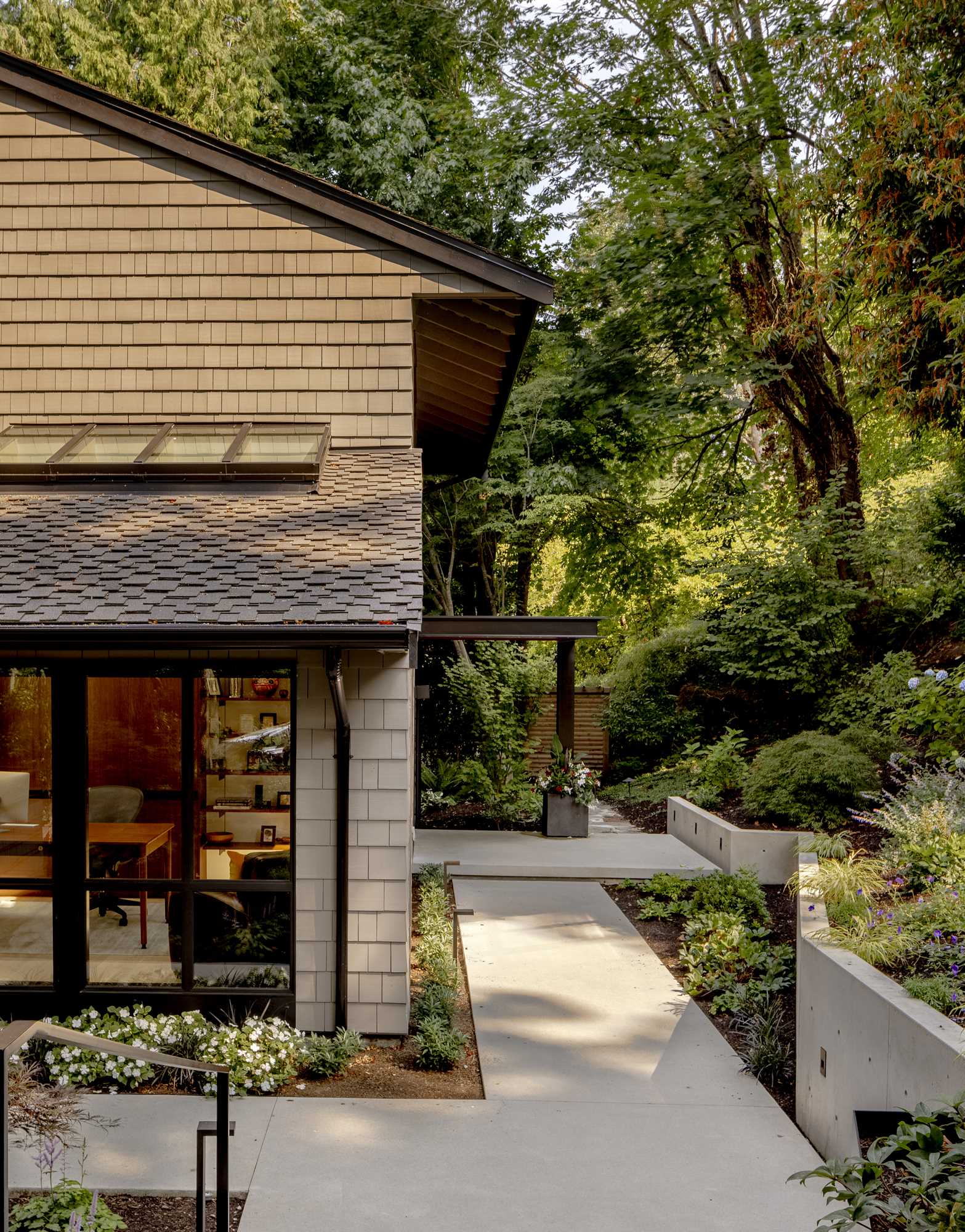 Concrete steps, steel planters, outdoor lighting, and angled landscape walls guide guests through the tree-filled property to the front door of this contemporary home.