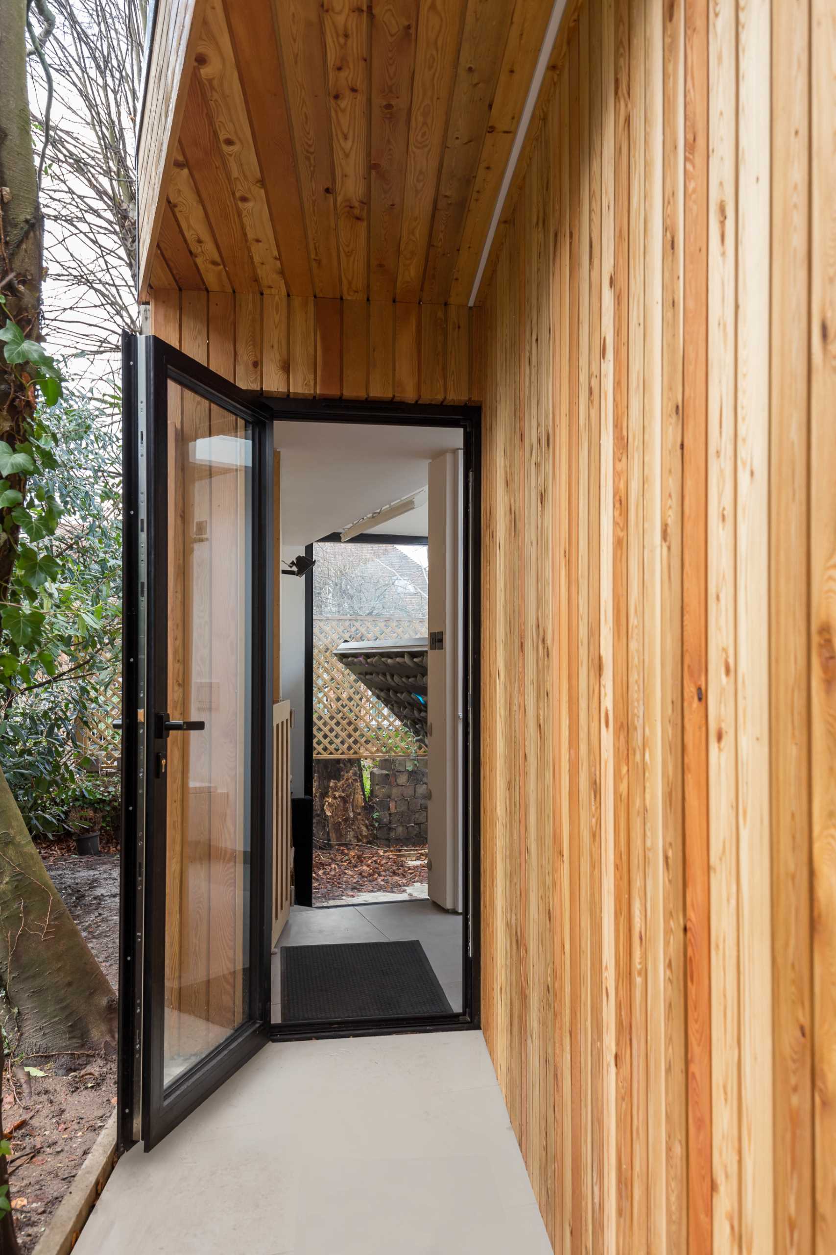 A small backyard home office and rock climbing gym is clad in wood and has black accents.